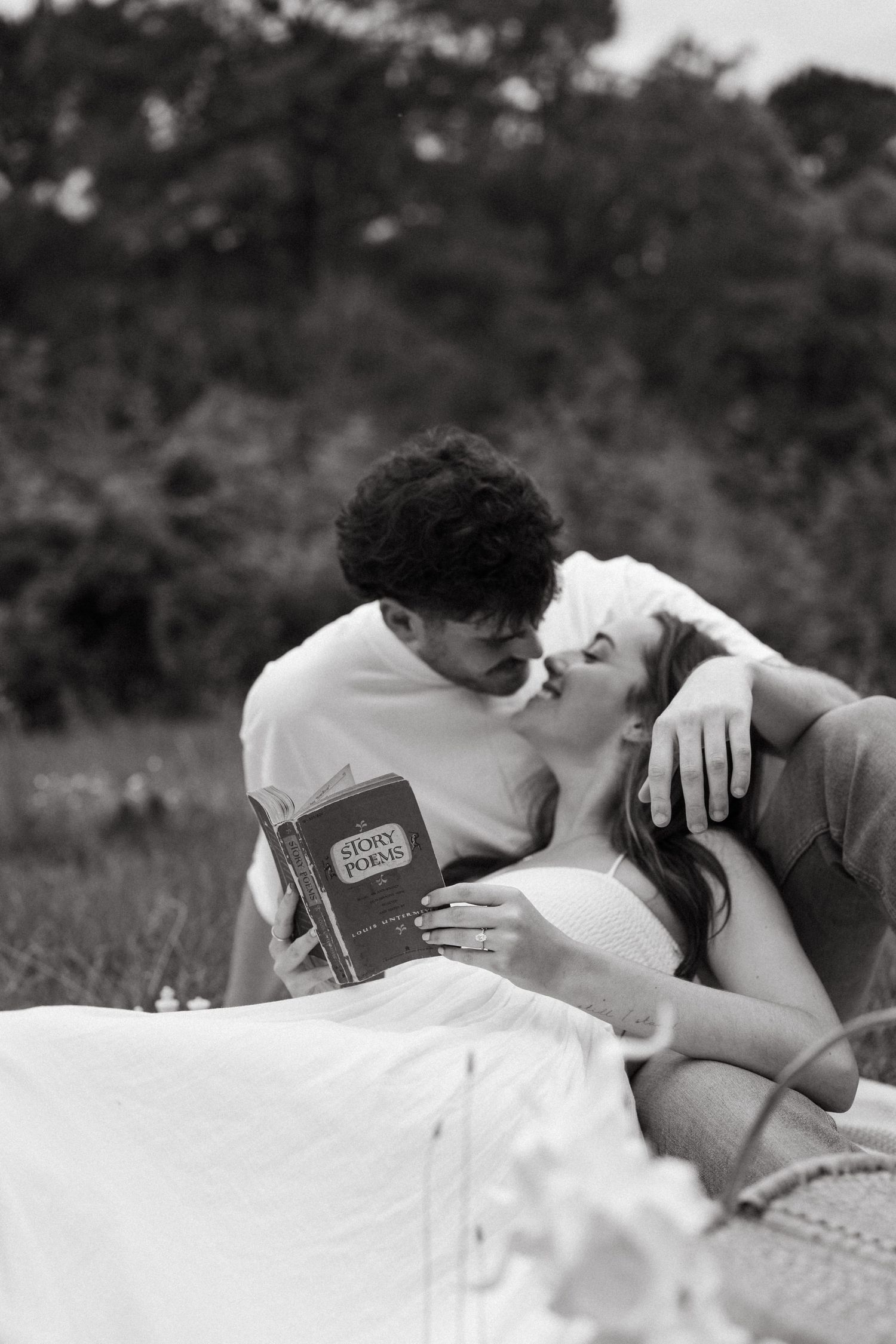 A romantic black and white photo of a couple sharing a tender moment while reading a book together outdoors.