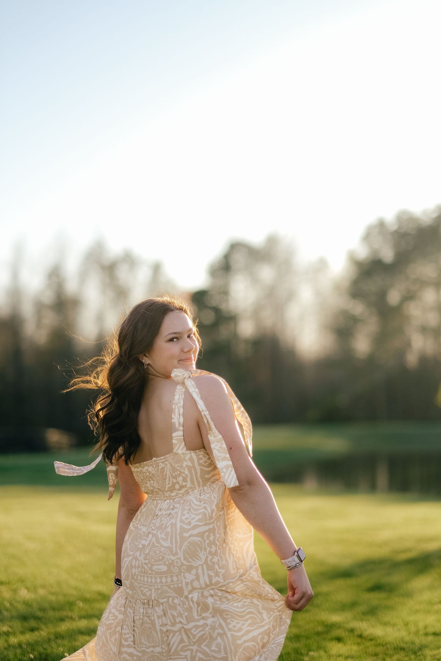 Dancing figure in a flowing white dress twirls joyfully in an open field at sunset.