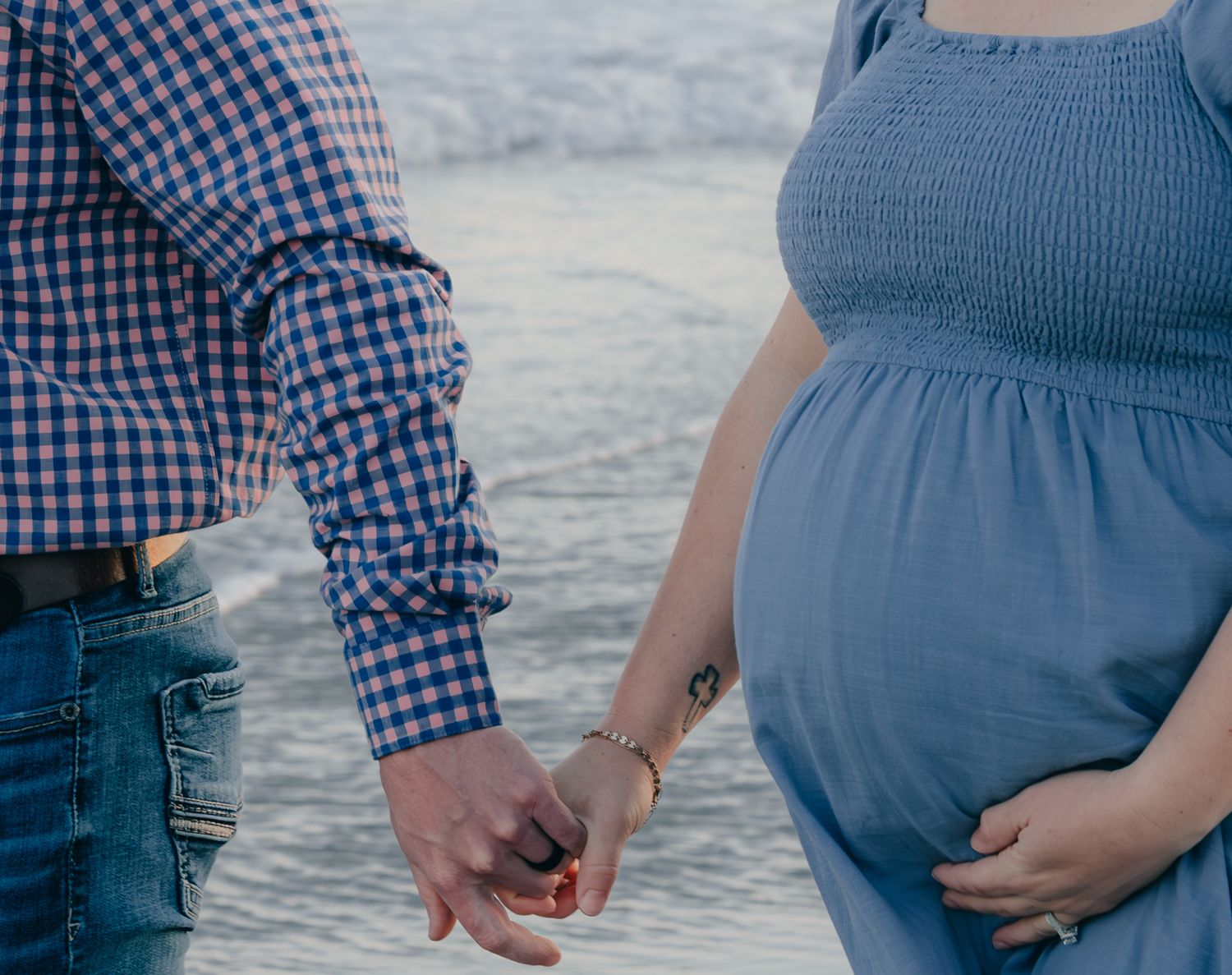 Close-up of couple holding hands at the beach with ocean in background.