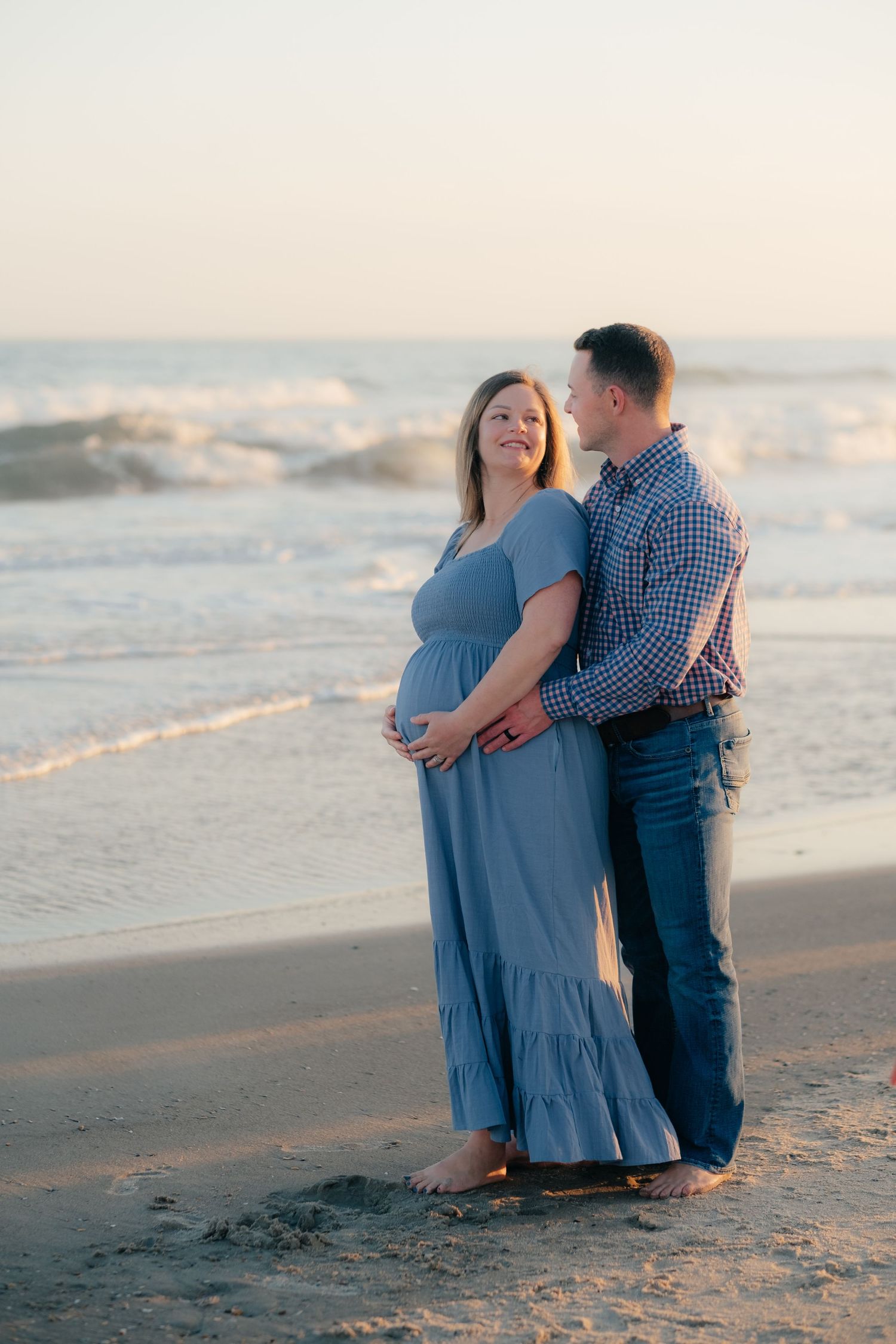 Couple sharing romantic moment on beach during maternity photoshoot.