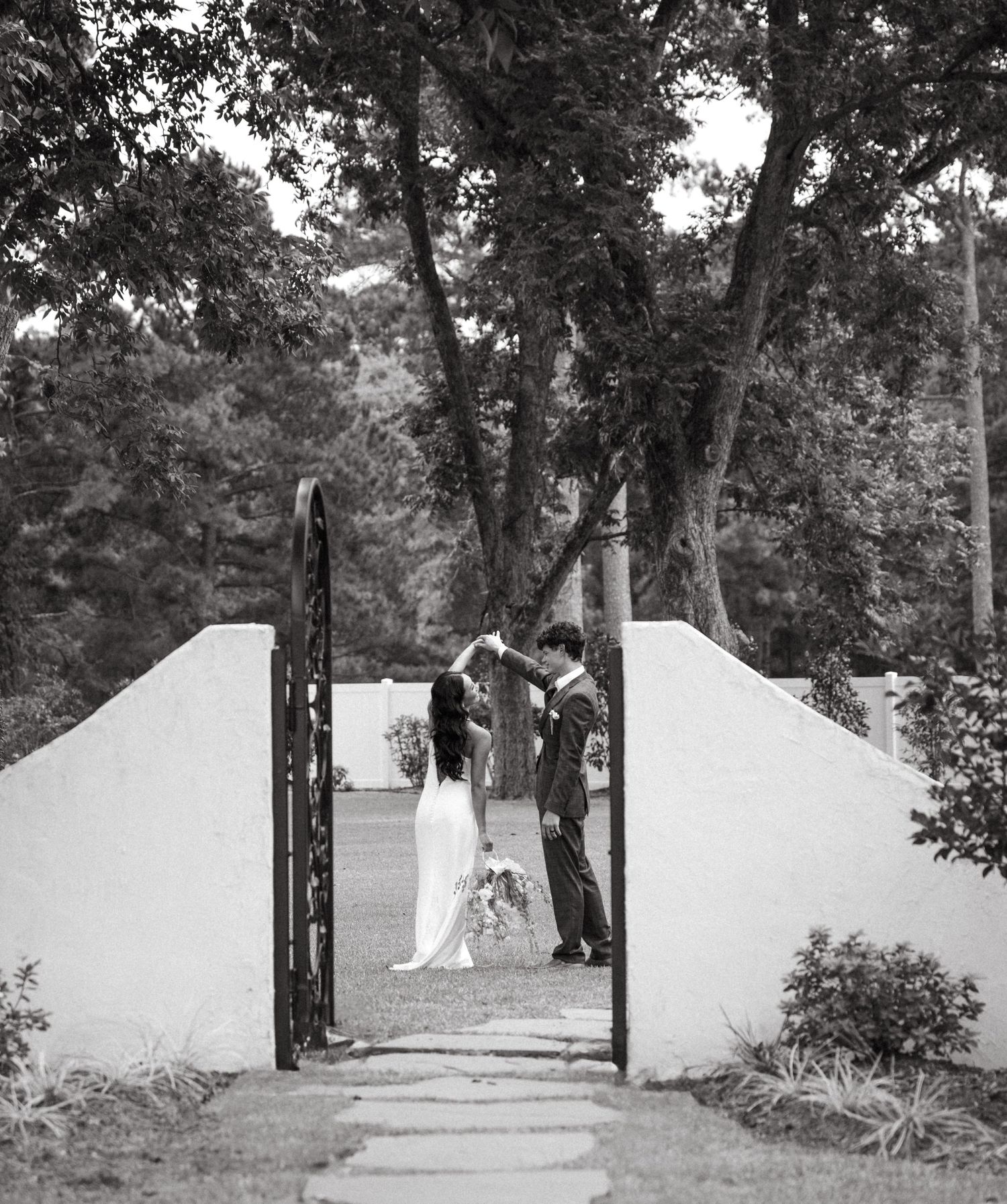 A black and white panoramic view of white walls creating a pathway through trees in an outdoor setting.