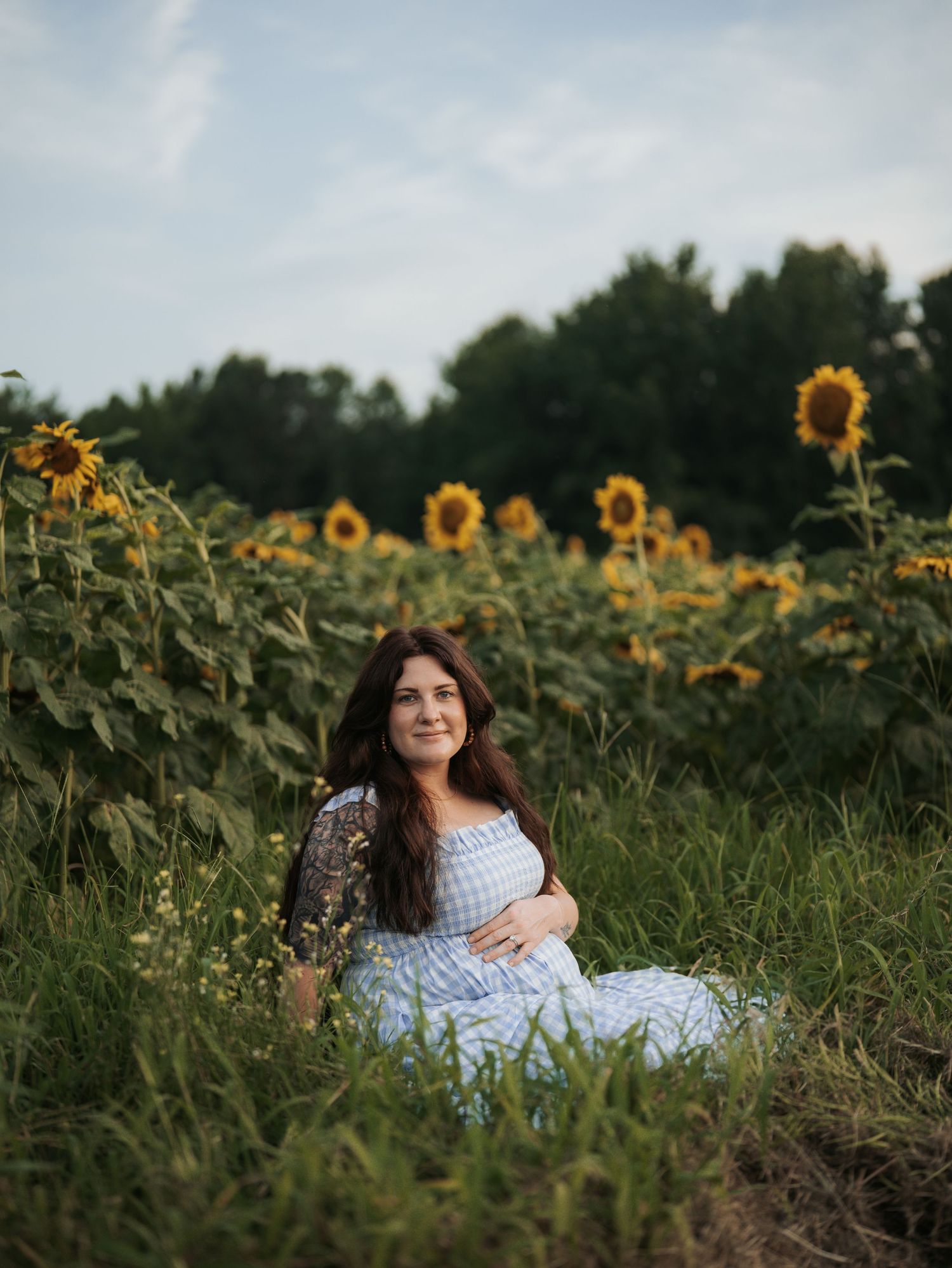 Woman in blue dress sits among blooming sunflowers in a summer field.