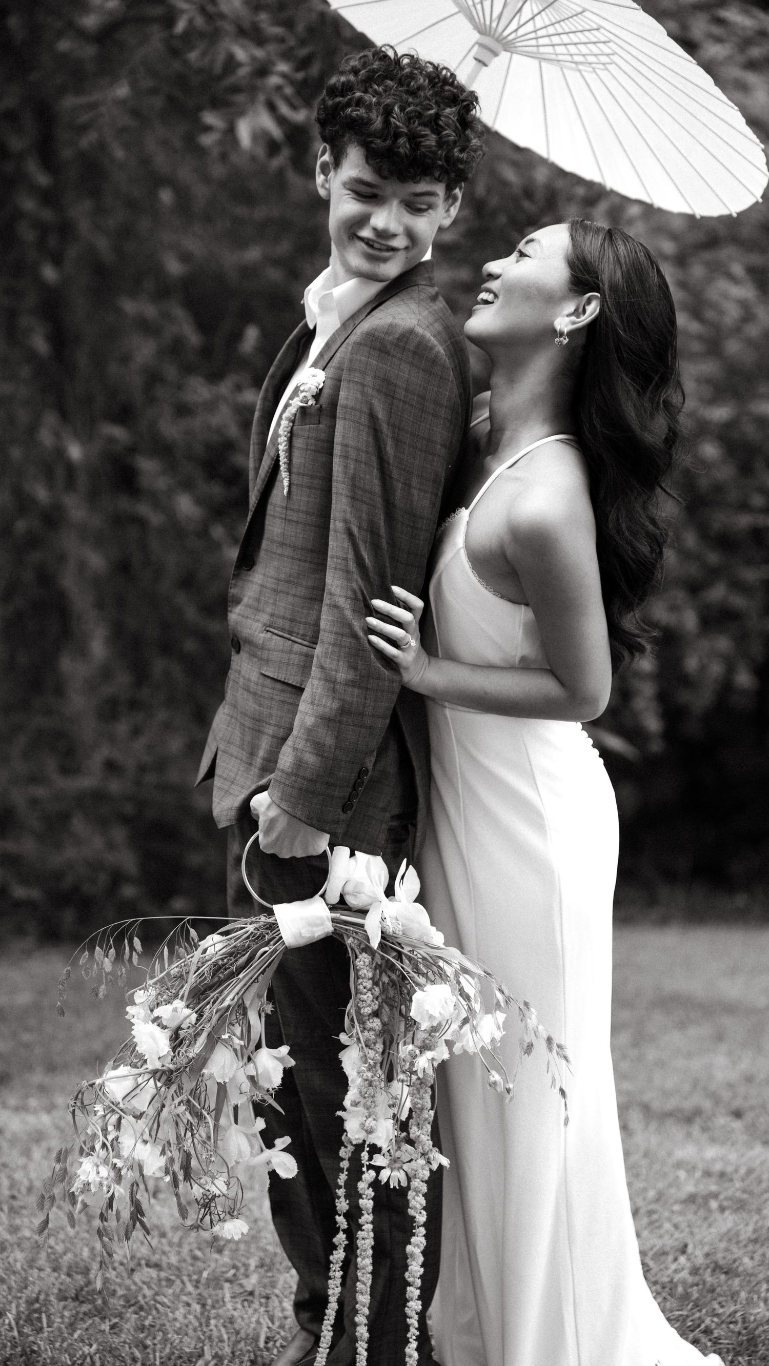 Black and white photo of couple with parasol in romantic garden setting.