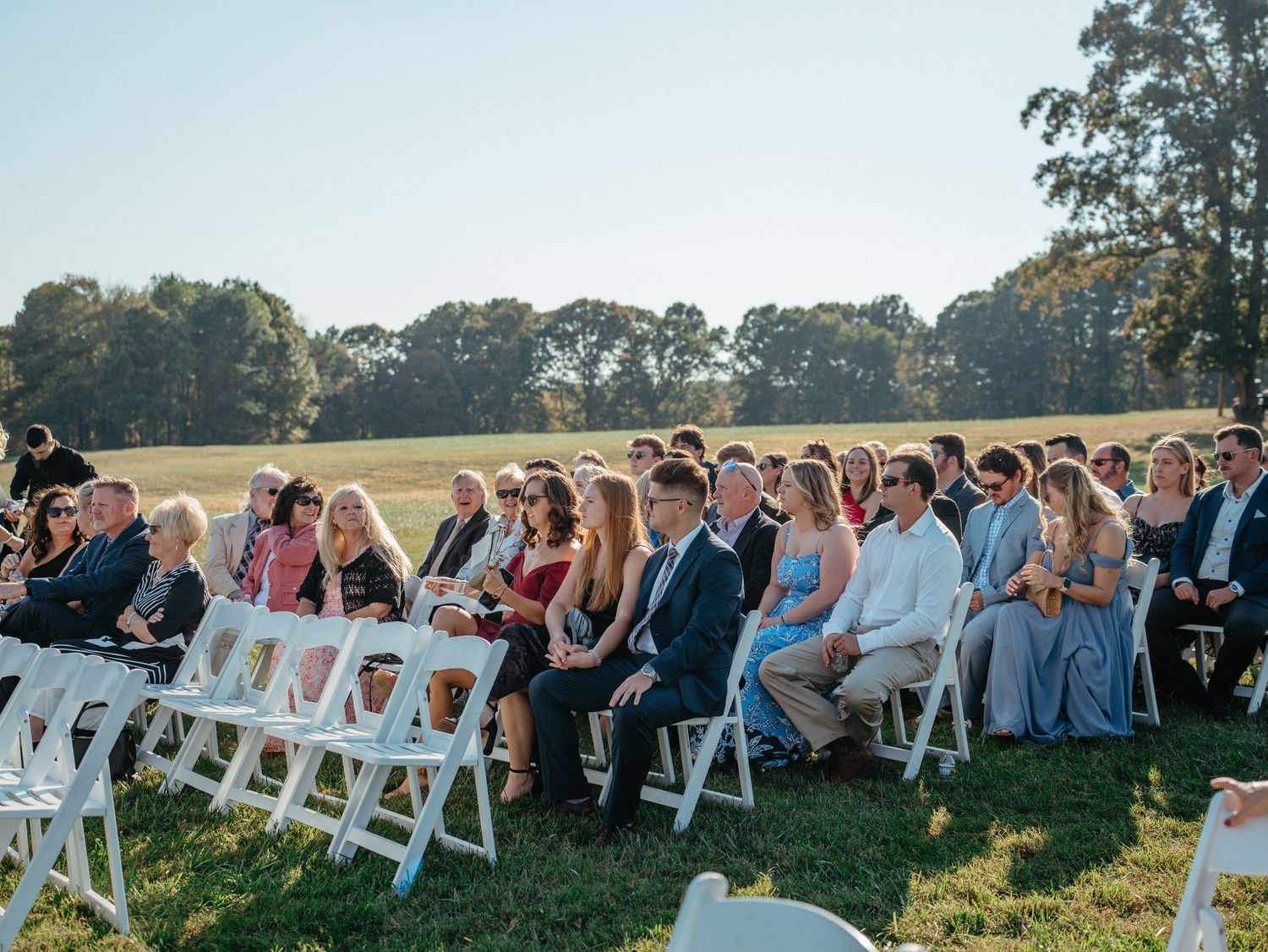 Rows of white chairs set up for an outdoor wedding ceremony with guests seated at sunset.