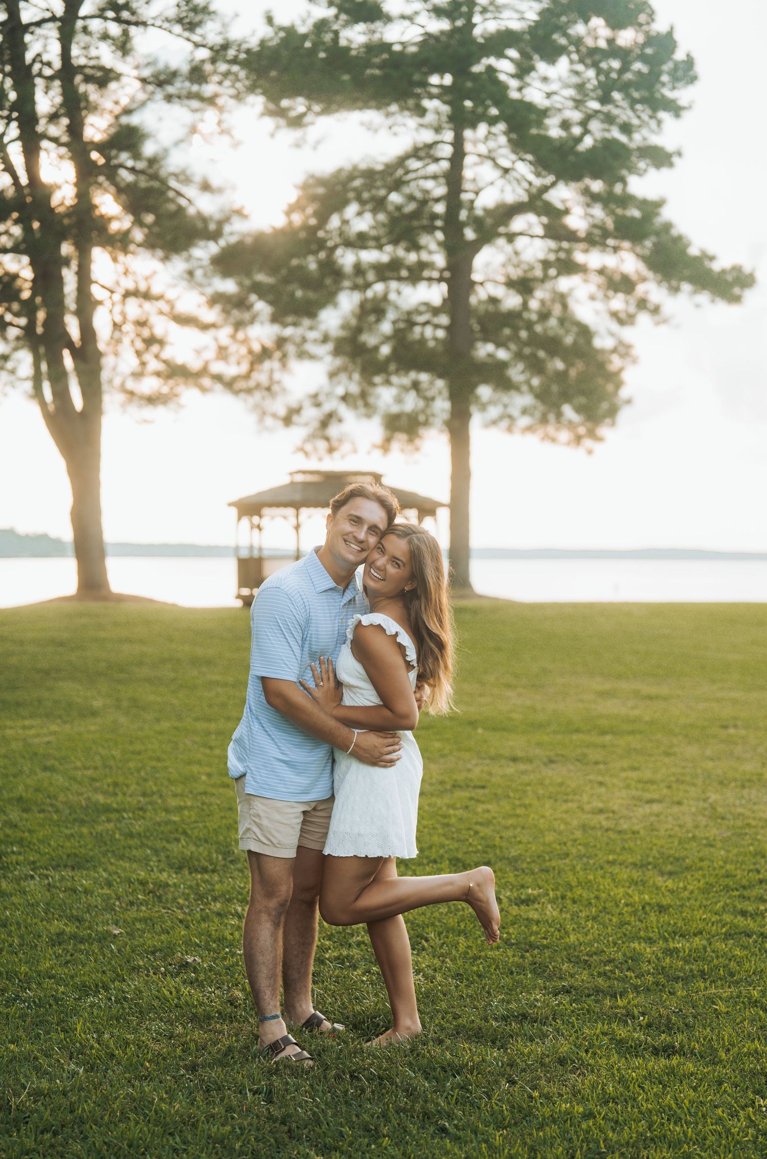 Couple shares tender moment on grassy hillside at sunset.