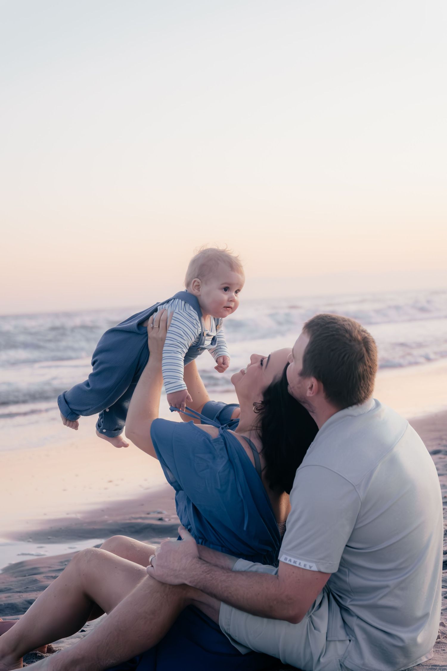Family playing and laughing together on beach at sunset.