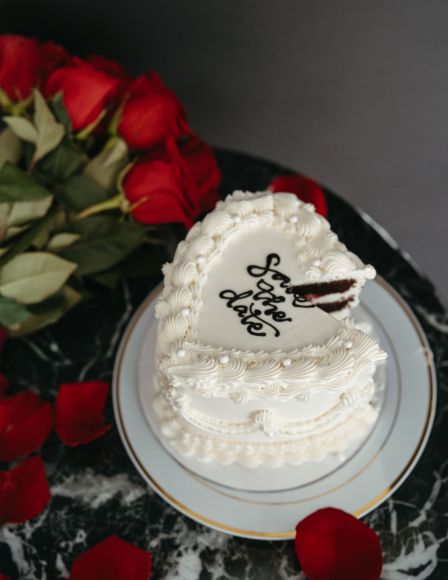White frosted cake decorated with pearls and text displayed with red roses.