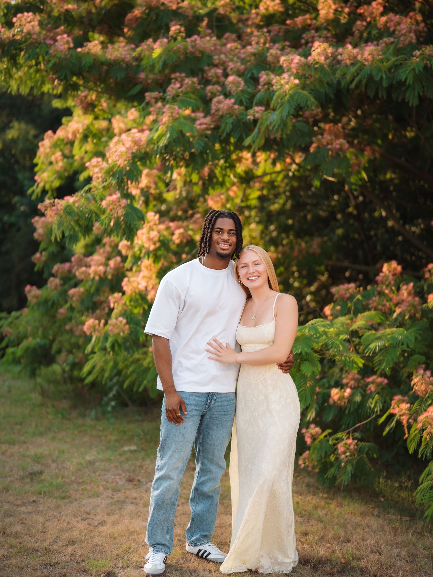 Couple posing together in front of blooming pink flowering trees in golden hour sunlight.