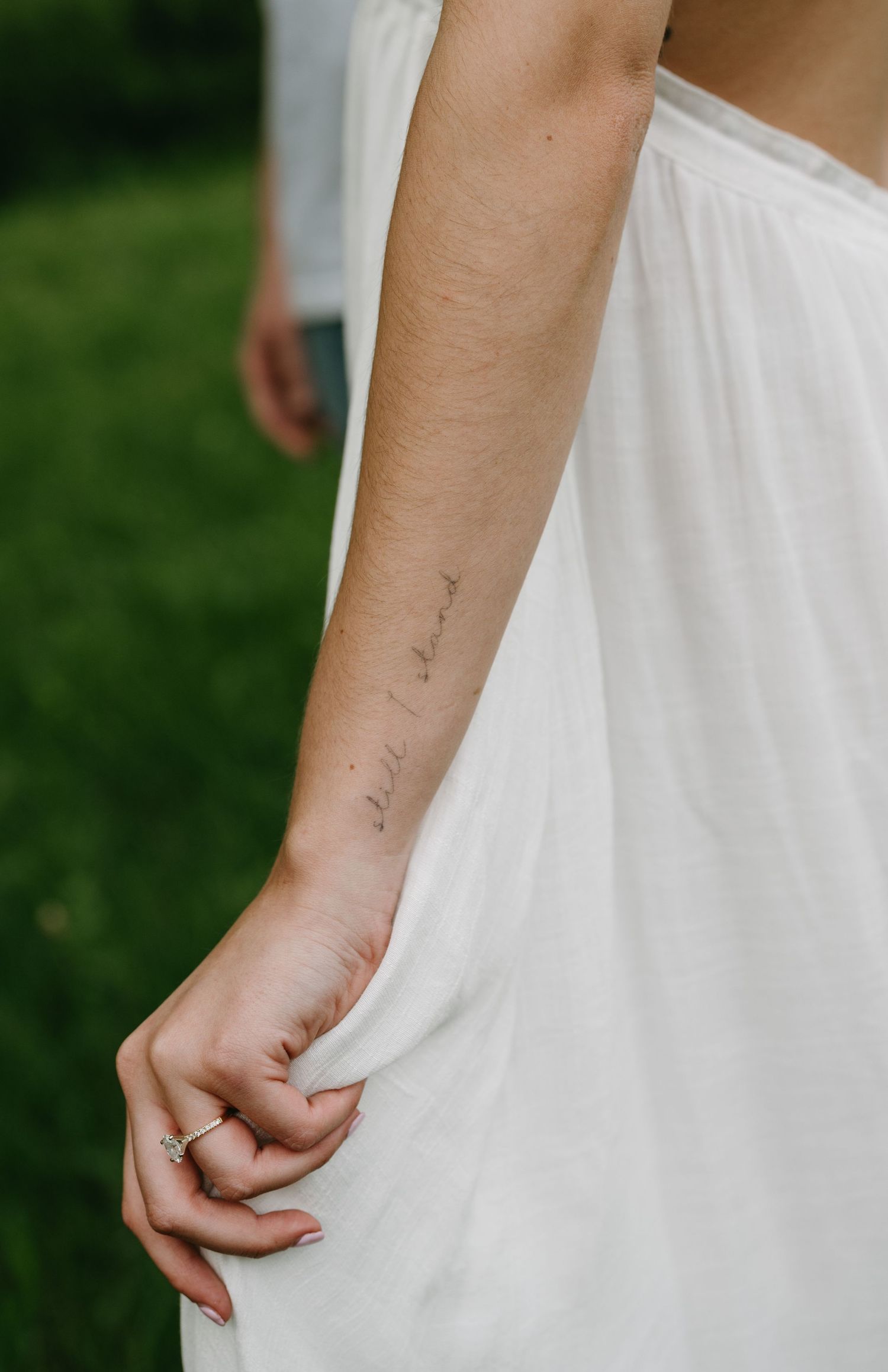 Close-up of delicate script tattoo on arm against white dress fabric.