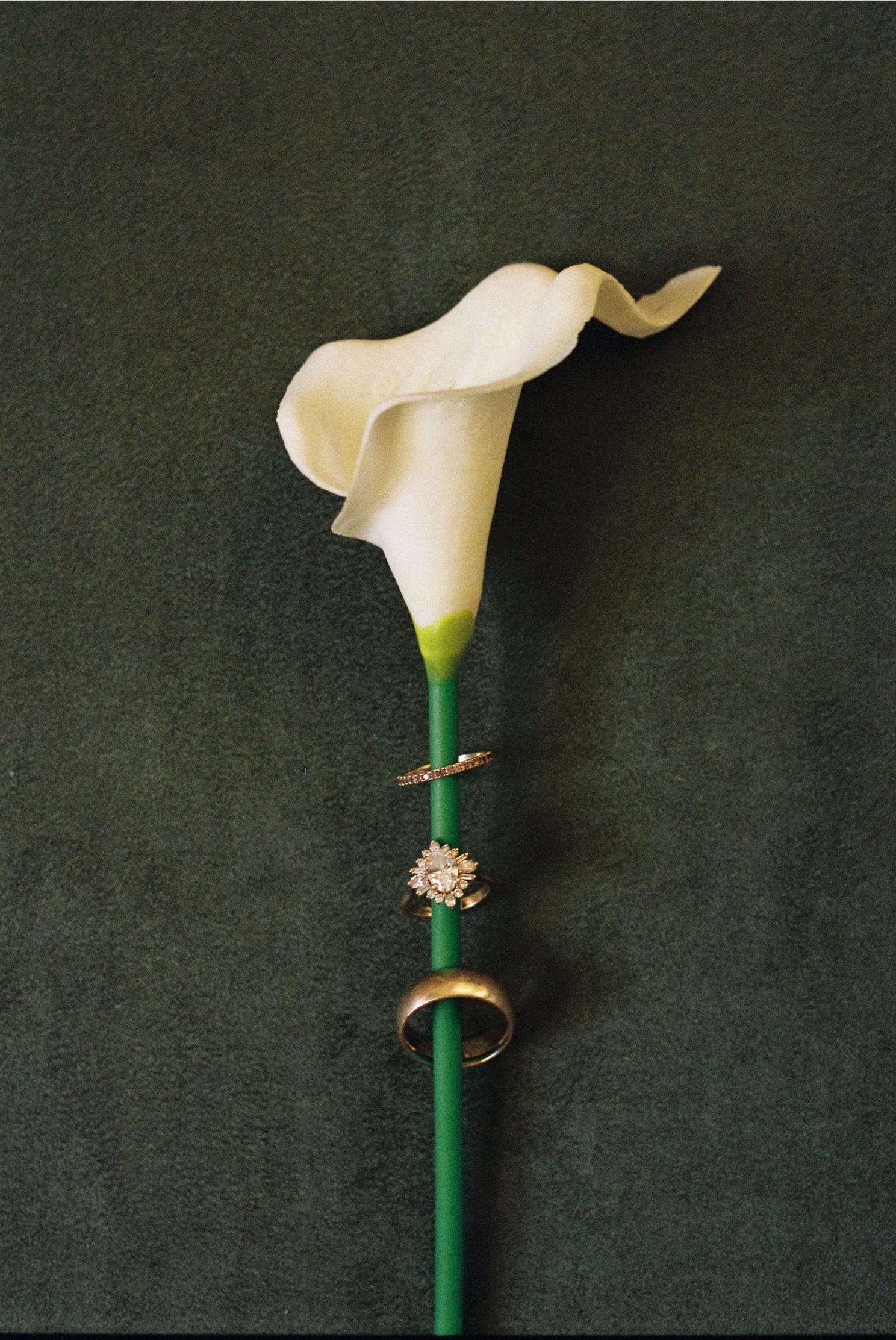 A white calla lily boutonniere with decorative pin against a dark green background.
