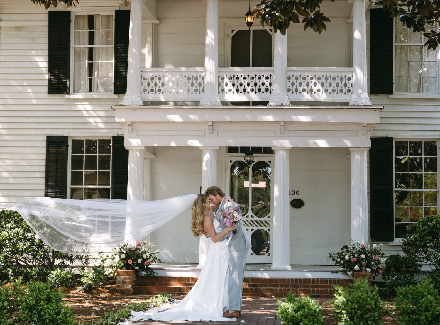 A classic white Southern mansion with wraparound porch features elegant columns and ornate railings in a traditional style.