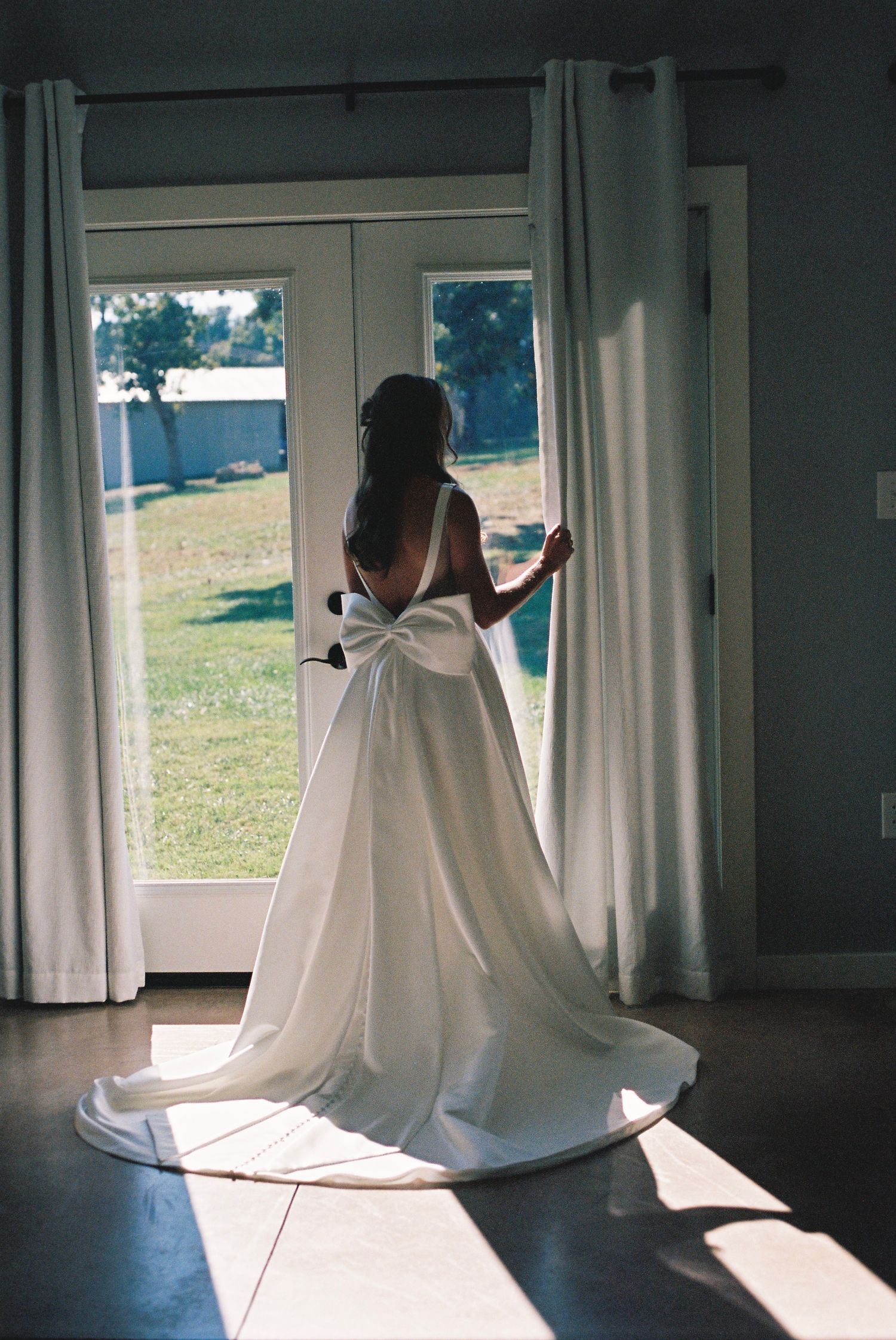 Ethereal silhouette of a wedding dress backlit by sunlight through white curtained windows.