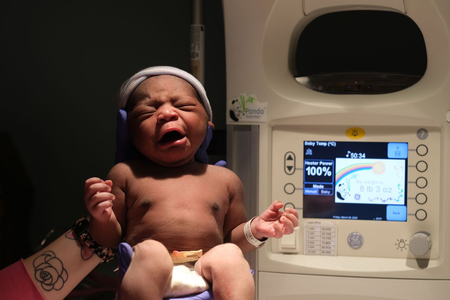 A newborn baby lies on a hospital bed under medical monitoring equipment.