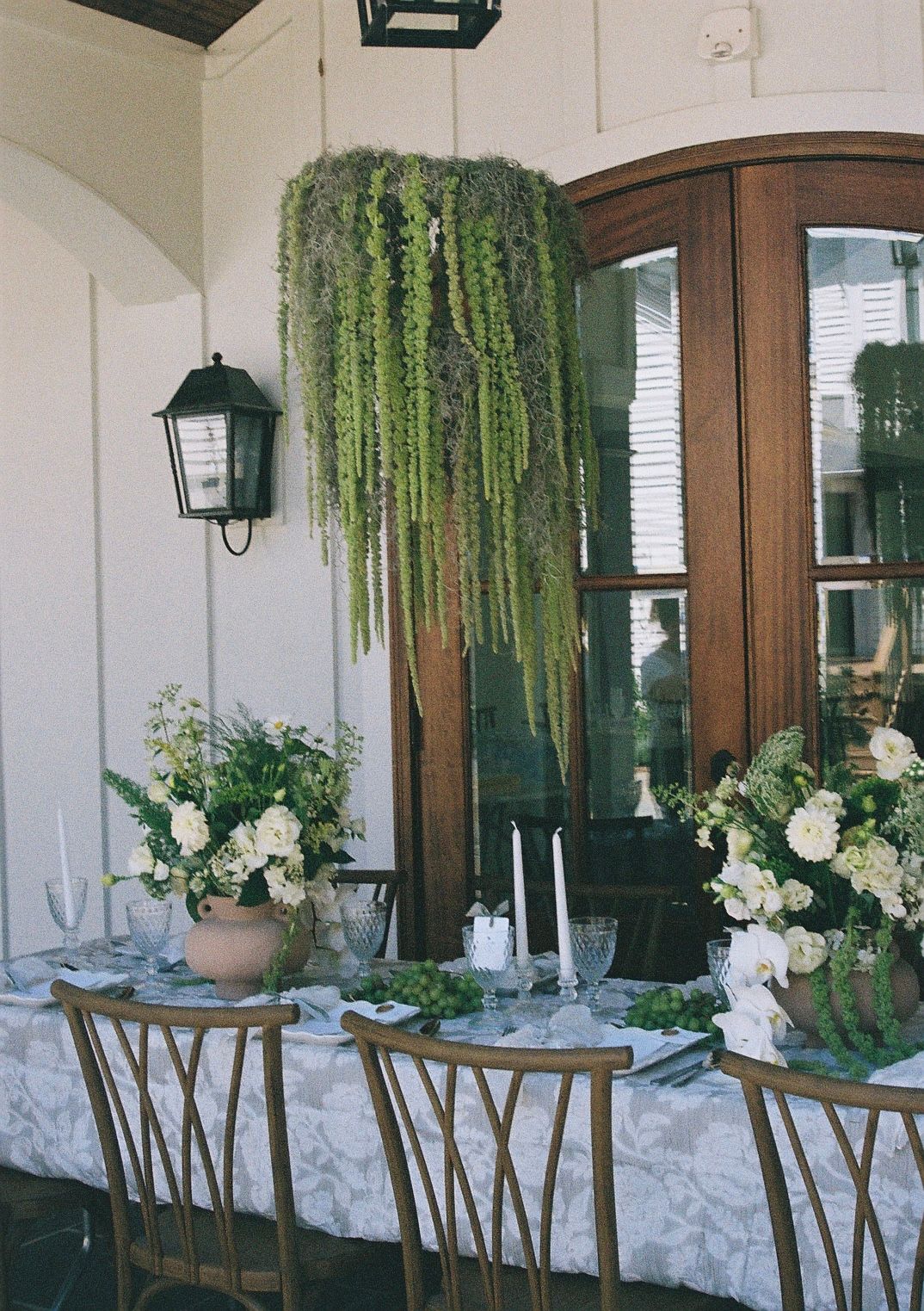 Wedding reception table decorated with hanging greenery, white flowers and wooden chairs.