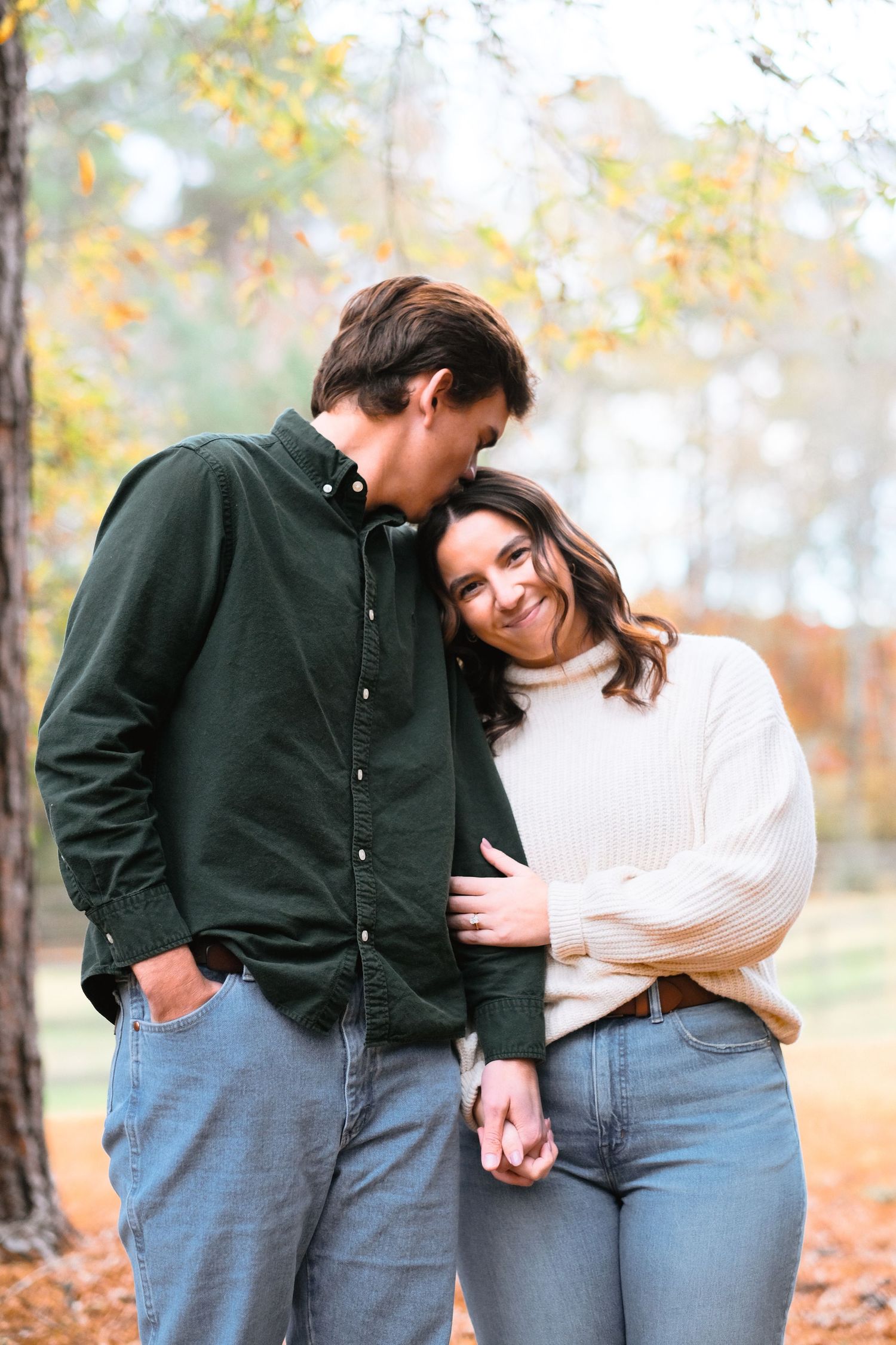 Romantic couple sharing tender moments among fall foliage in matching denim and sweaters.