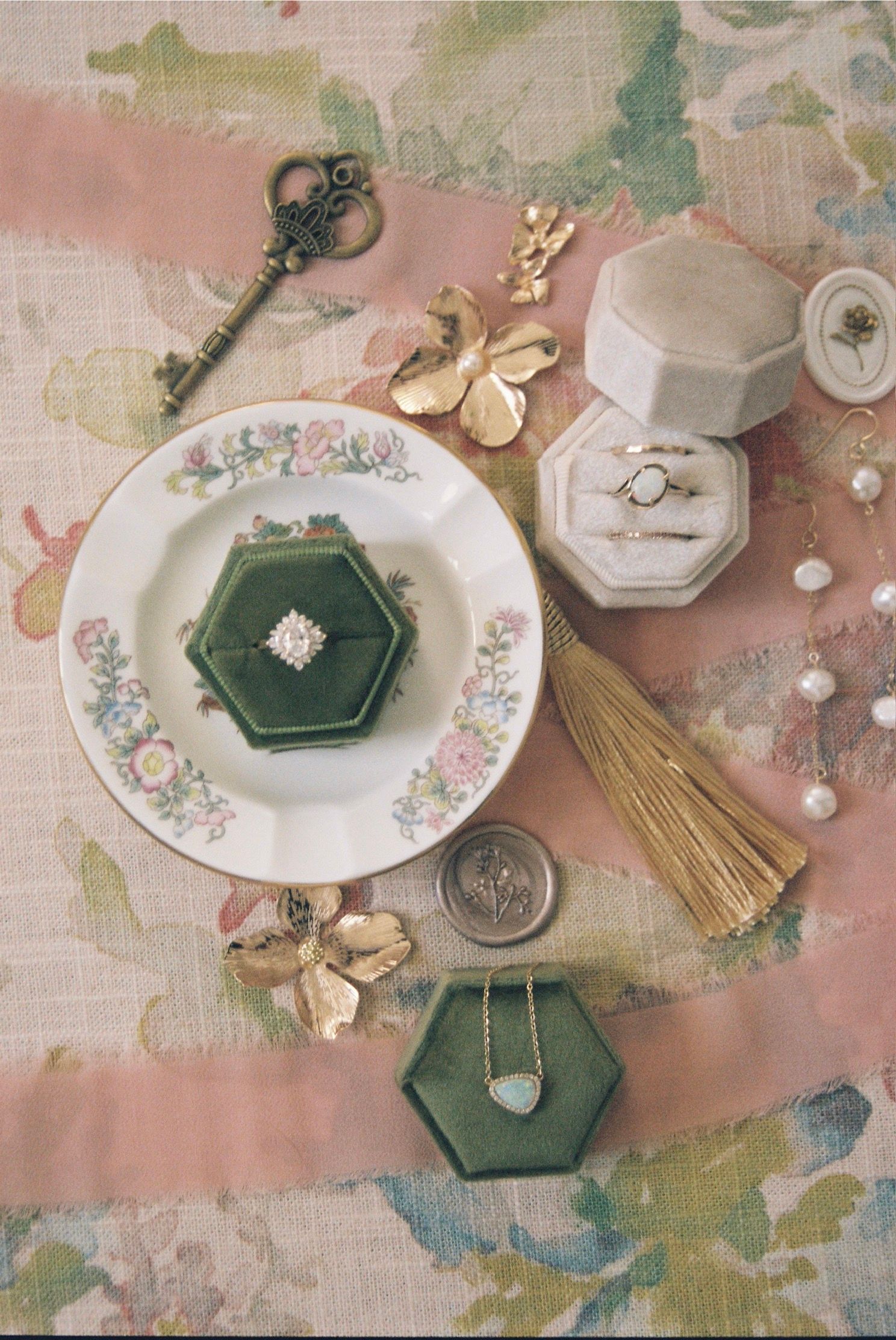 Vintage floral plates and decorative green hexagonal boxes arranged with delicate gold butterfly accents on a pastel surface.