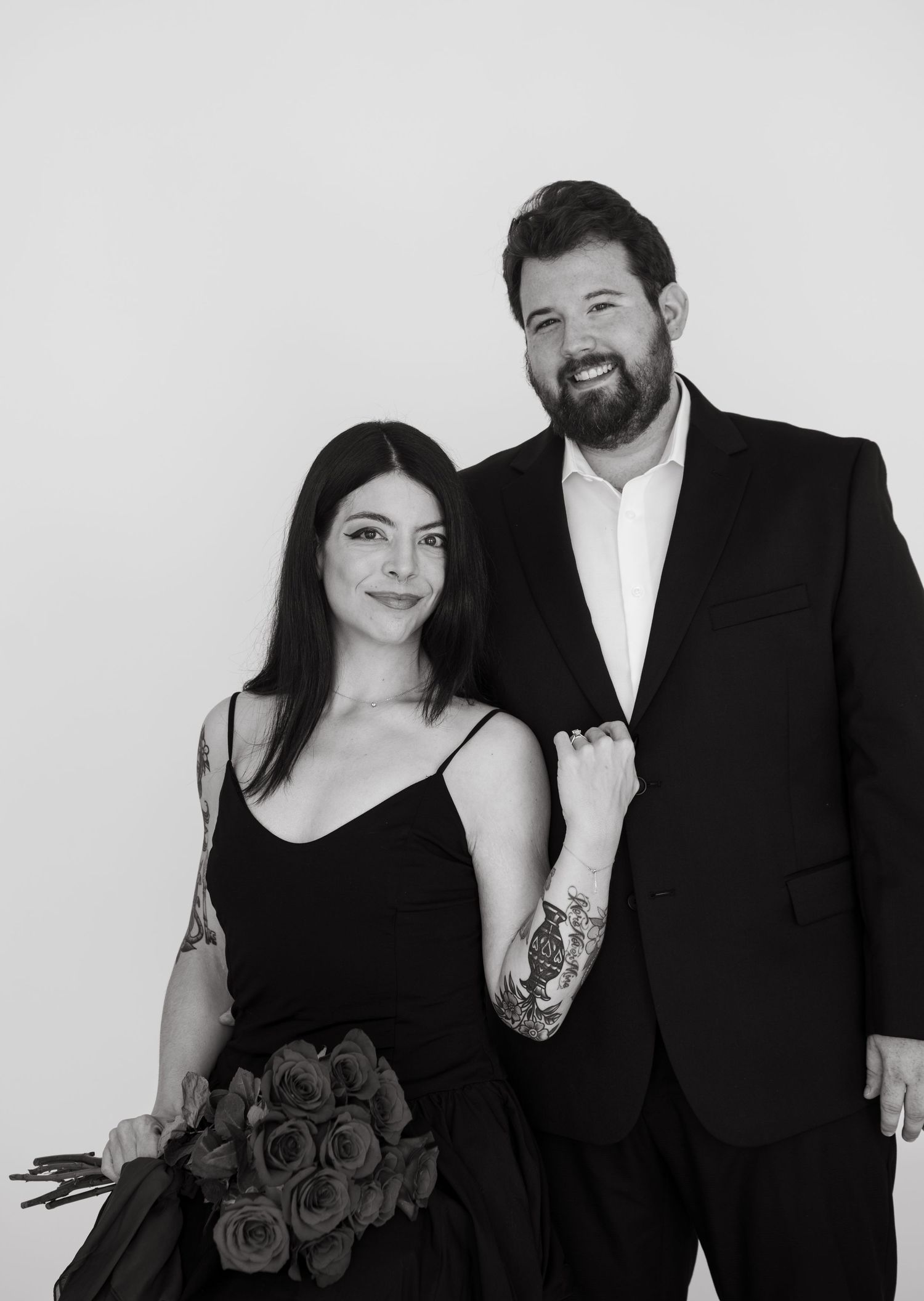 Elegant couple in black formal wear poses for studio portraits with red roses.