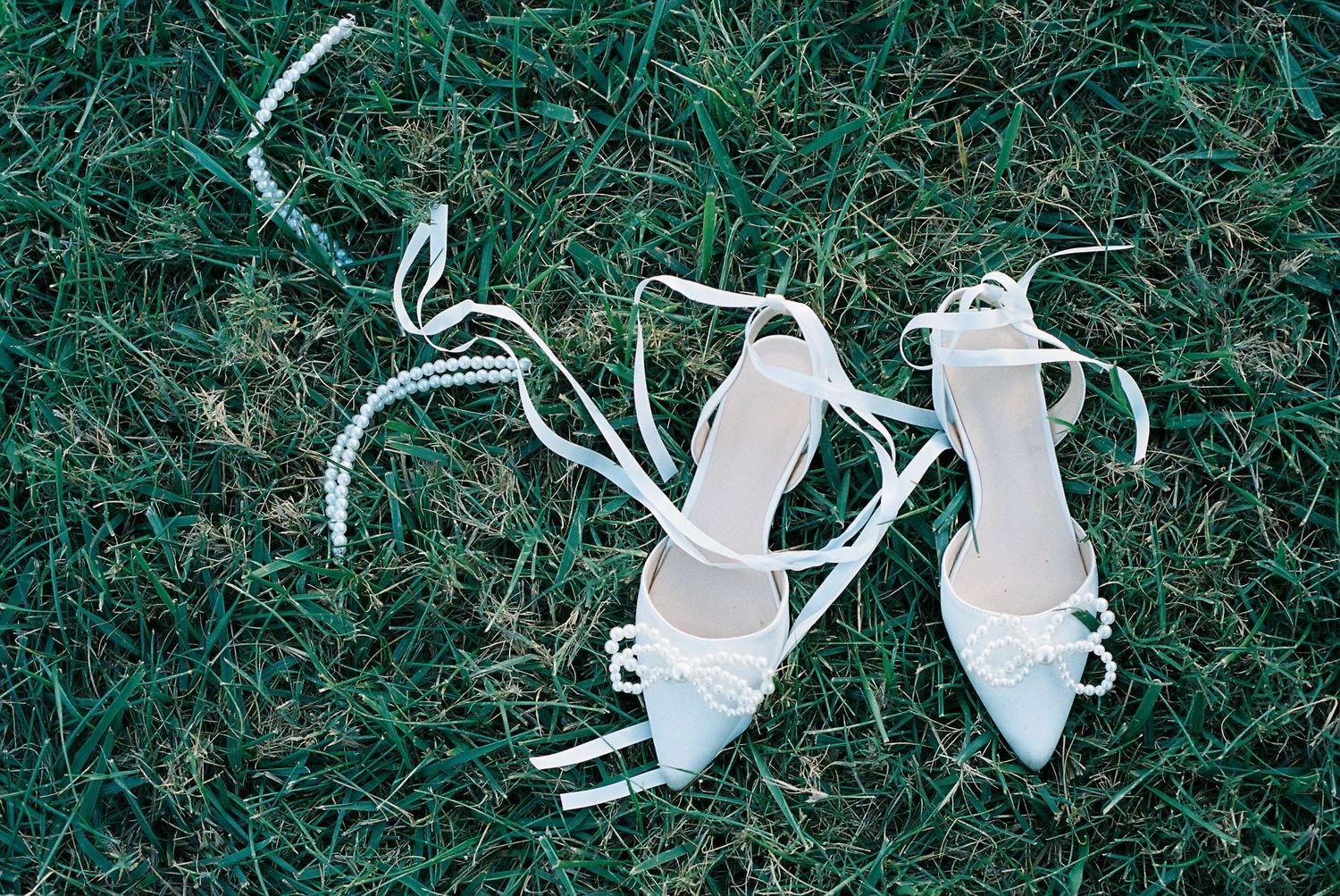 White wedding shoes arranged on green grass in a series of artistic shots on film.