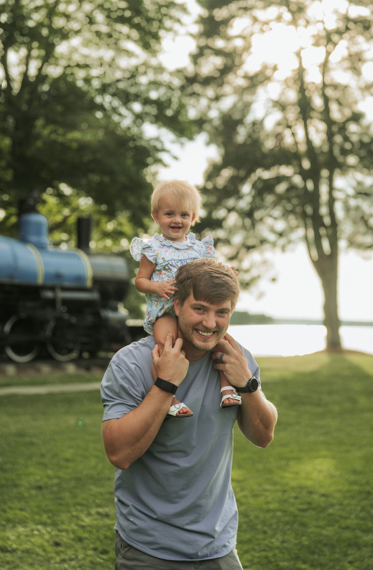 Joyful playtime with toddler riding on shoulders in park during golden hour.