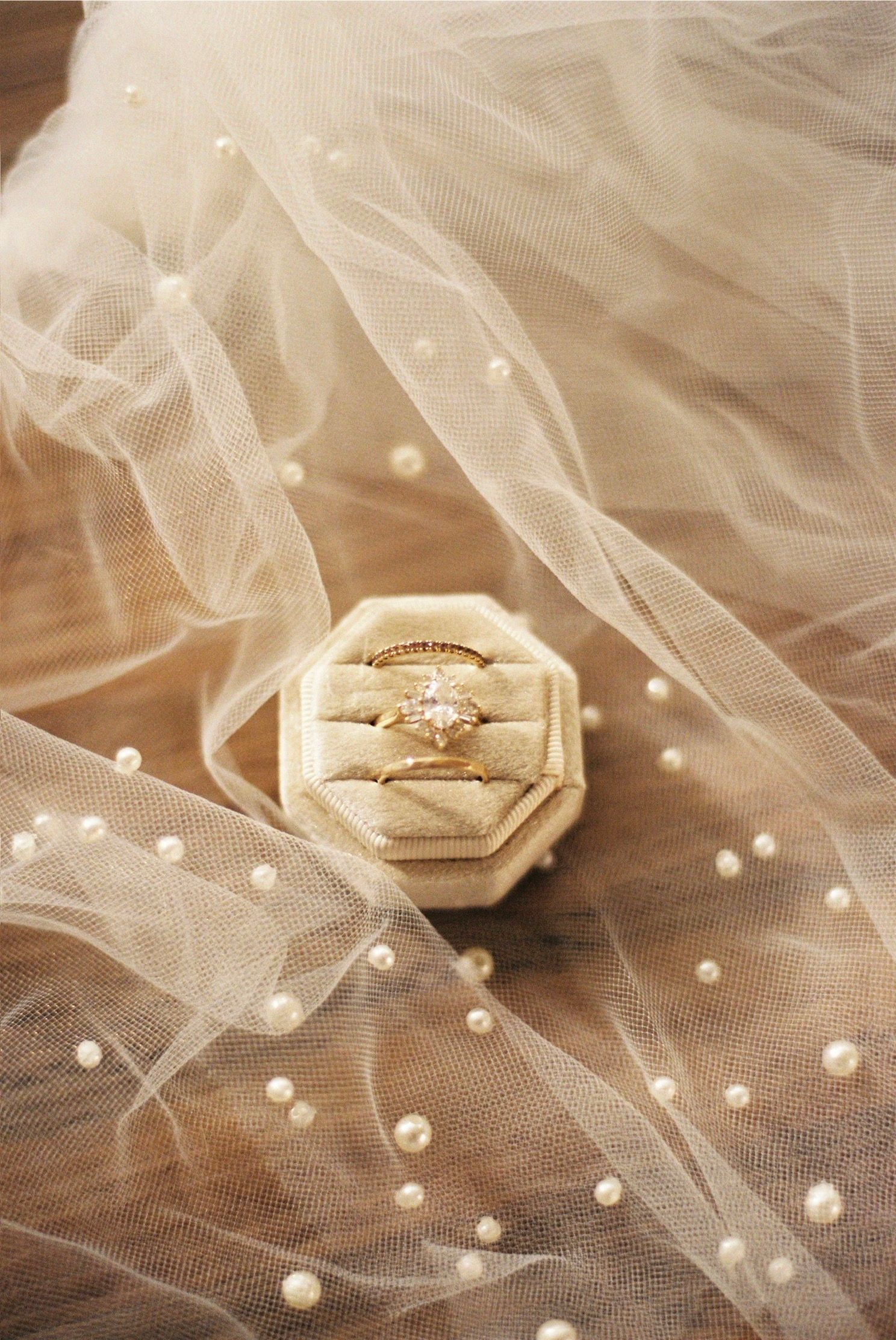 Elegant engagement ring displayed on delicate pearl-dotted tulle veil with soft lighting and romantic bokeh effect.