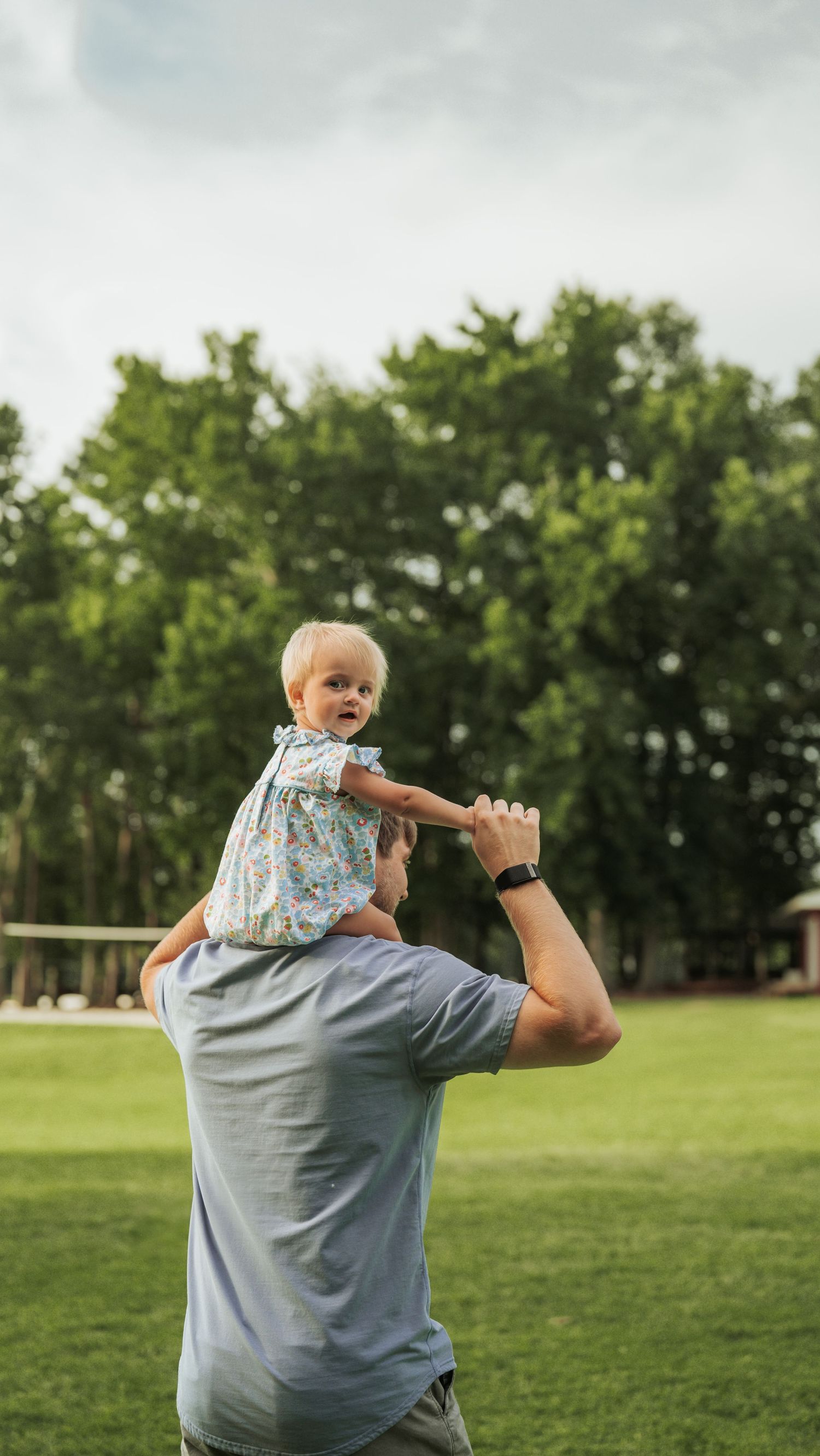 Parent playfully lifts small child in the air on a grassy lawn during golden hour.