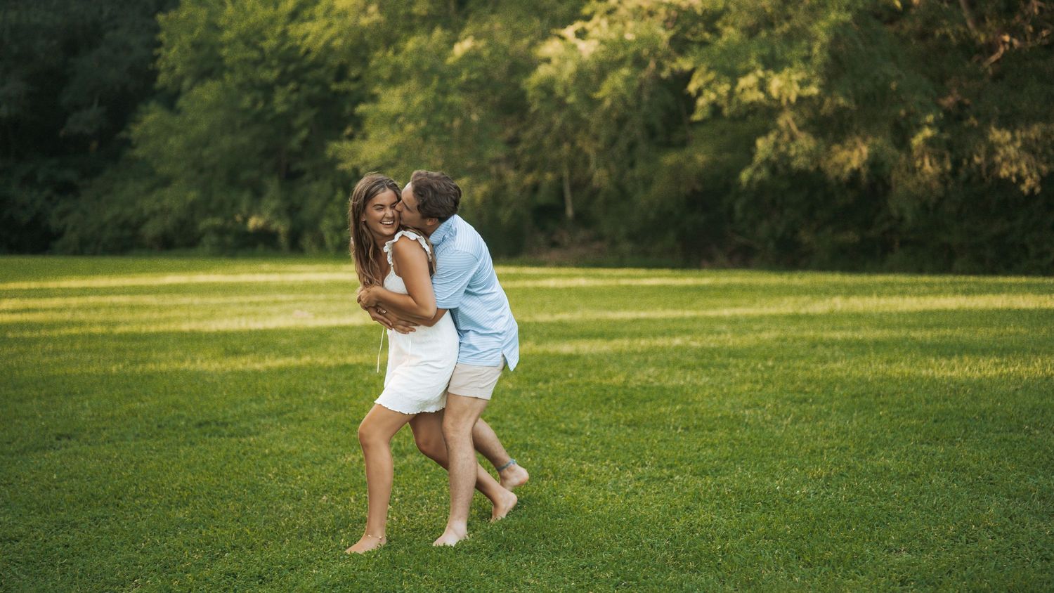 Playful couple running and dancing on a sunlit green lawn.