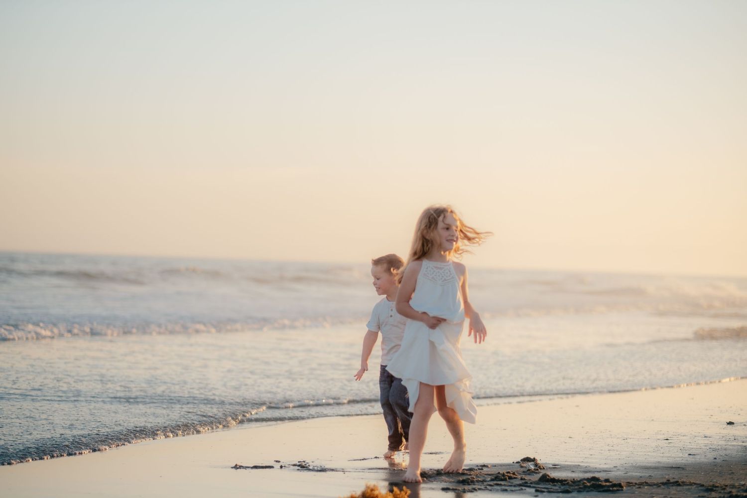 Family enjoying a sunset beach photoshoot in white and blue outfits near the ocean waves.