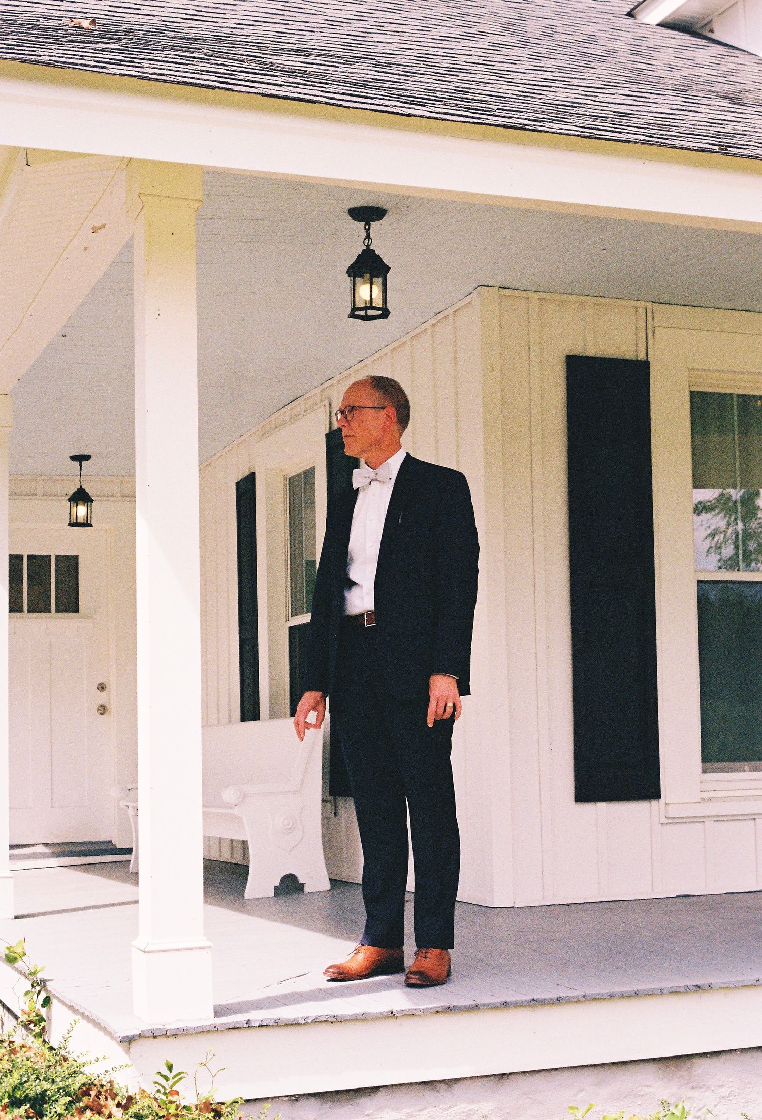 Wedding party members gather on a white colonial-style porch with classic columns.