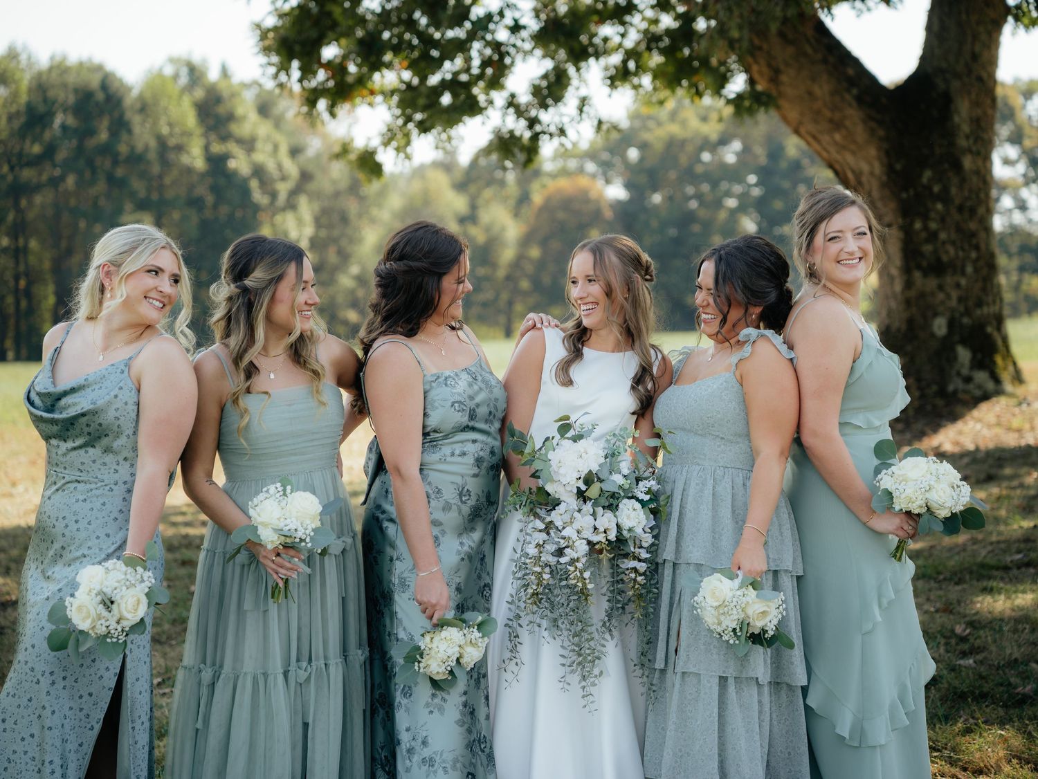 Bridesmaids in light blue dresses holding white bouquets under trees.
