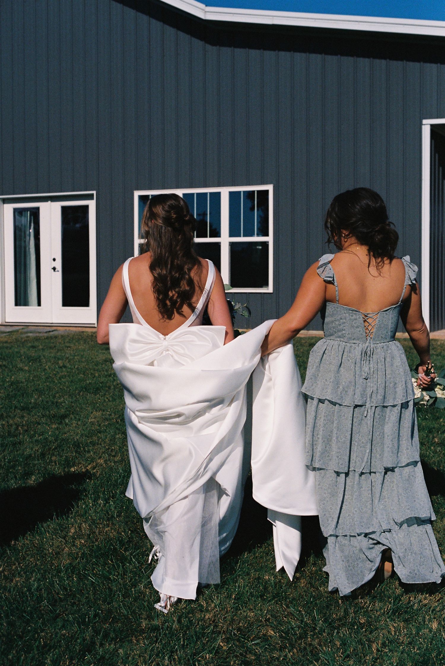 Row of bridesmaids in white dresses and gray shawls standing together outdoors.