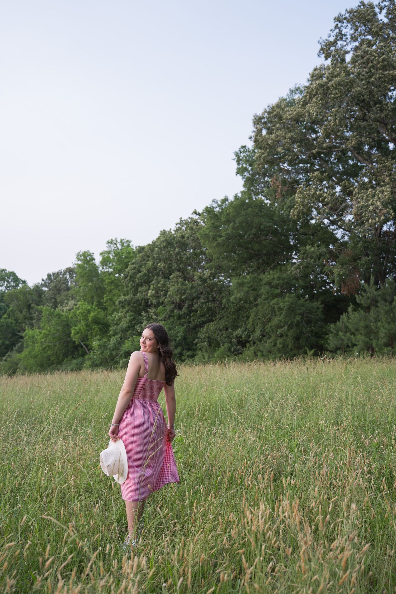 Figure in pink dress walking through a sunlit meadow with trees in background.