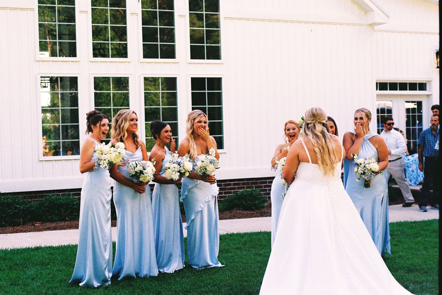 Wedding party members in light blue dresses and white gowns standing outdoors.