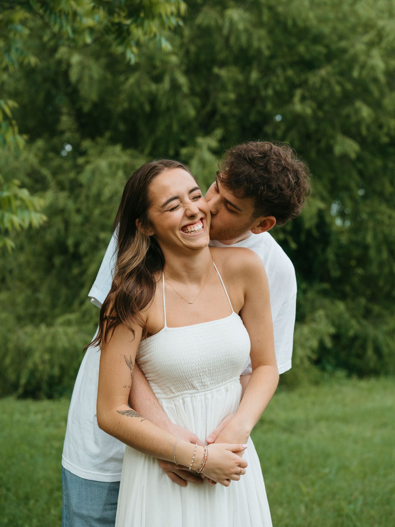 A romantic couple shares tender moments in a sunny outdoor setting wearing white.