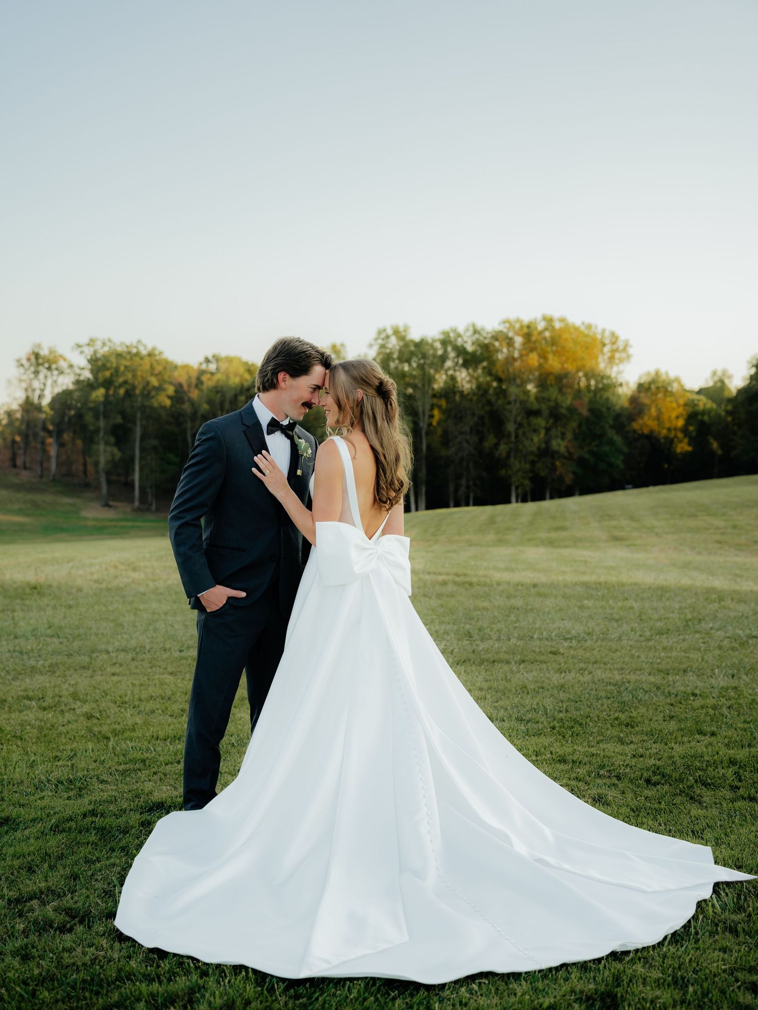 Romantic sunset portrait of a couple in wedding attire on a rolling green hillside.