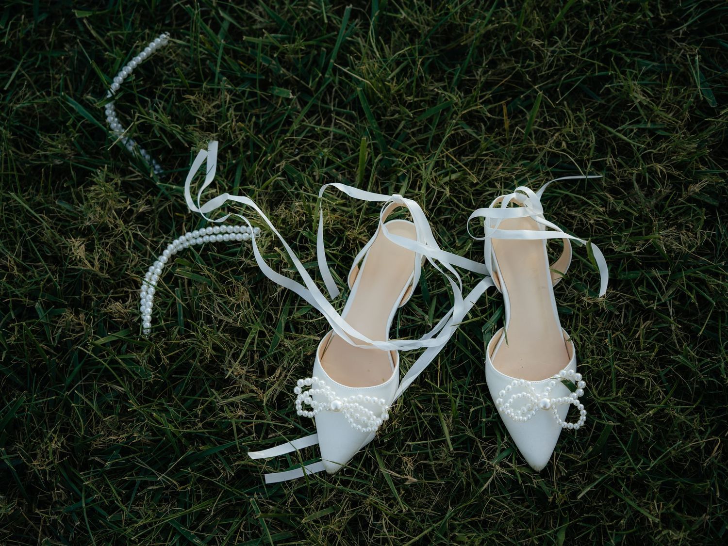 White bridal shoes placed on dark grass creating elegant contrast.