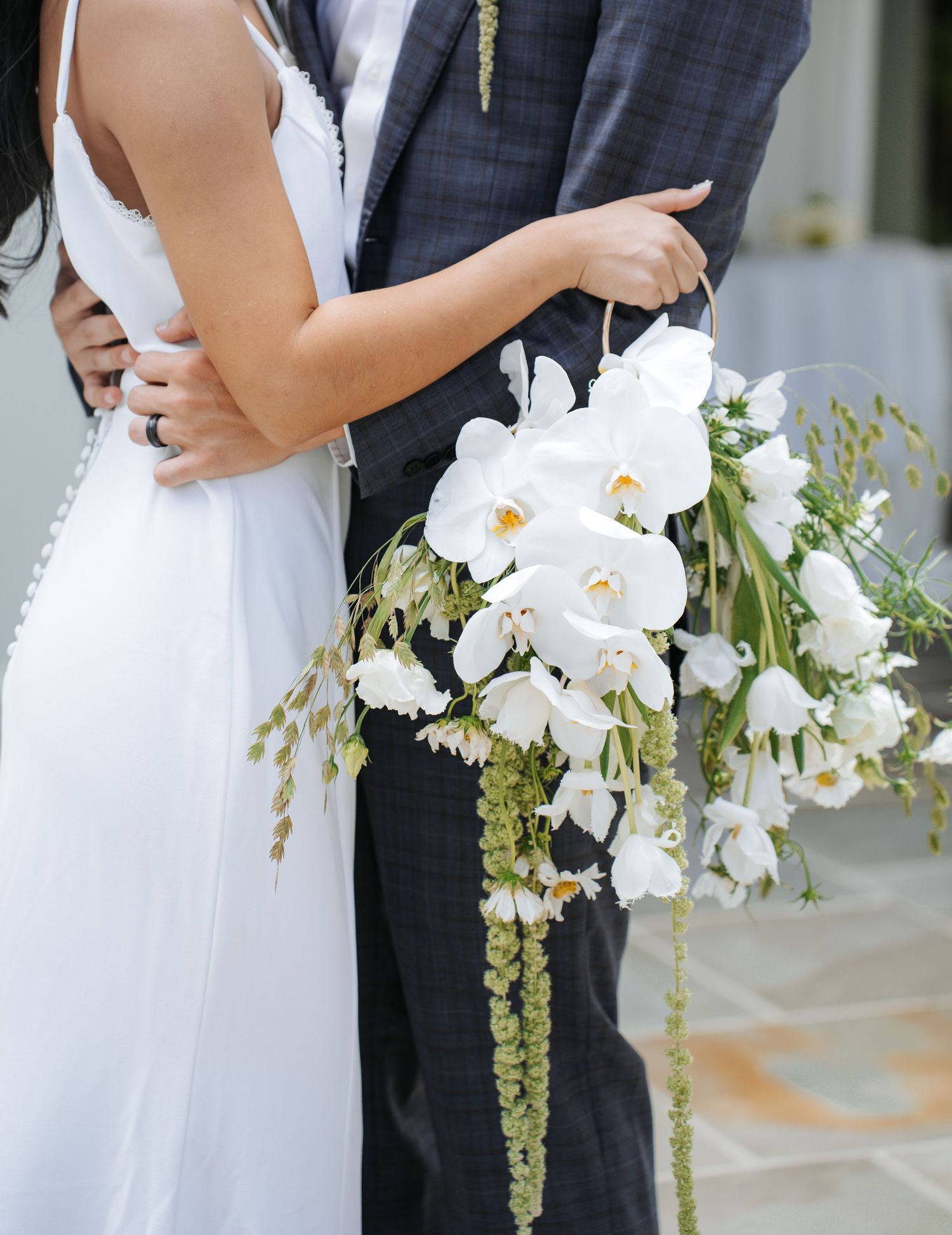Elegant white floral bouquet with cascading greenery held against formal wedding attire.