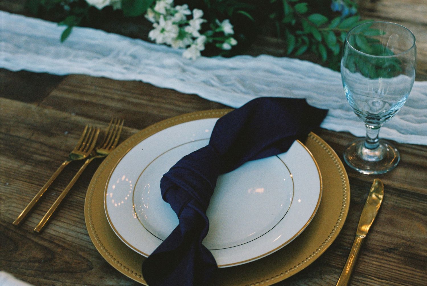Elegant place setting with navy napkin, gold charger, and crystal stemware.