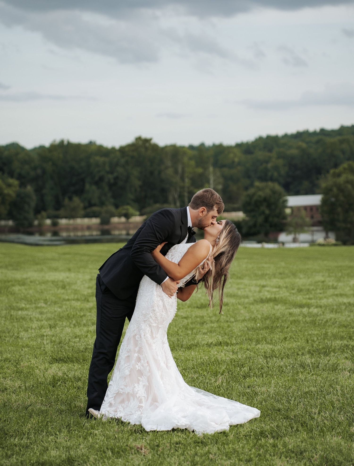 Bride and groom share romantic dip pose in grassy field during wedding photoshoot.