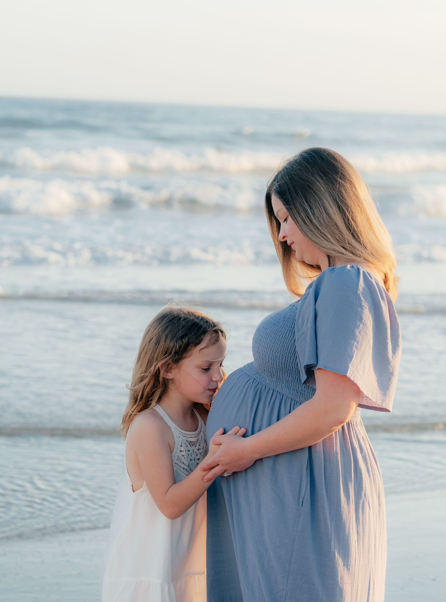 Touching moment between mother and daughter during beach maternity session.