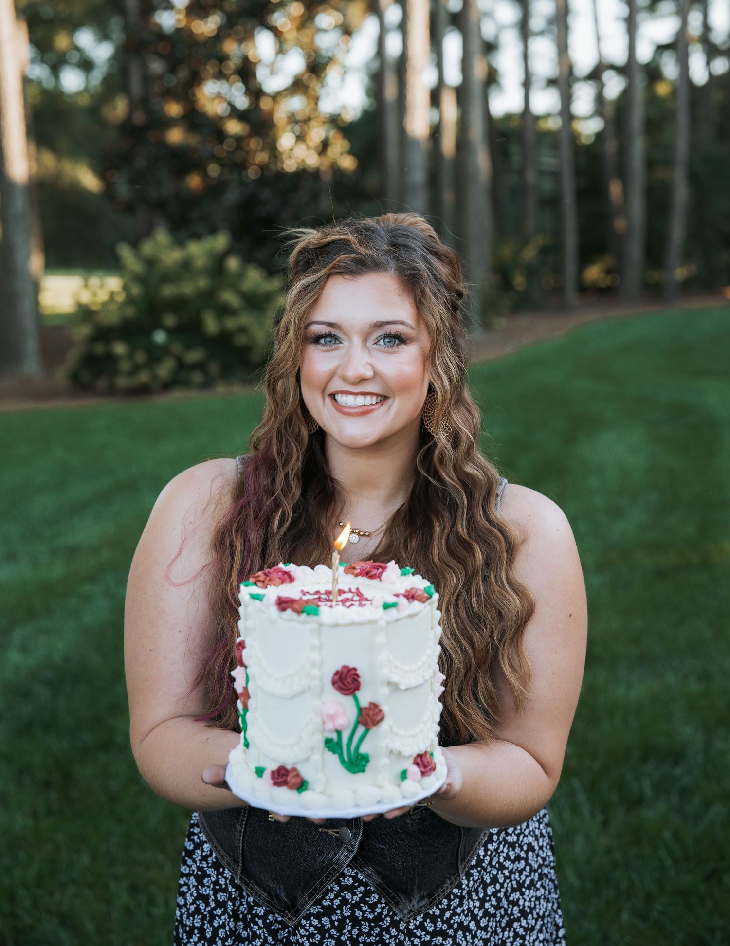 Person holding a white frosted cake decorated with red berries outdoors.