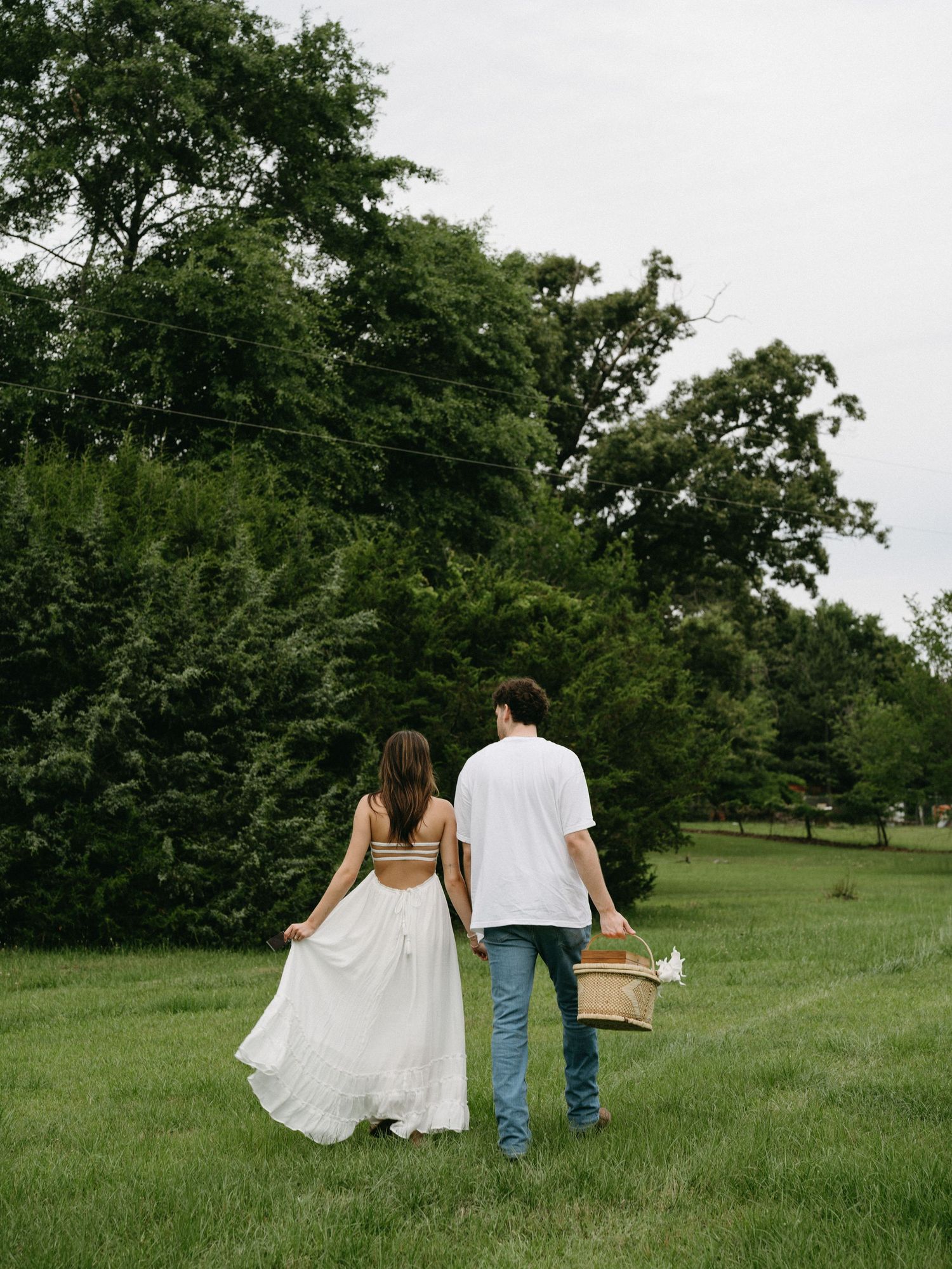 A couple walks hand in hand across a green field on a summer day.