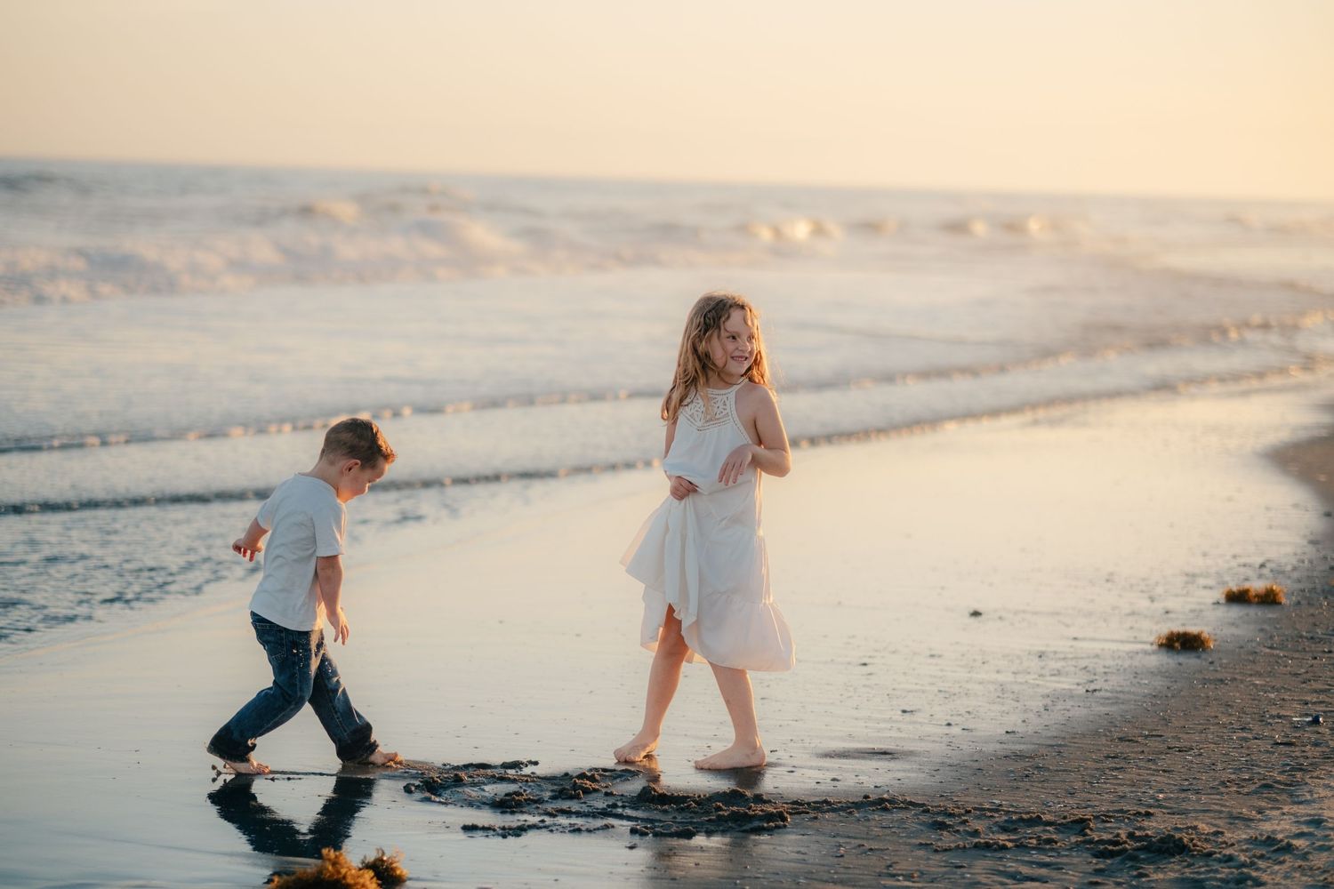 Children playing joyfully along the ocean's edge during sunset.