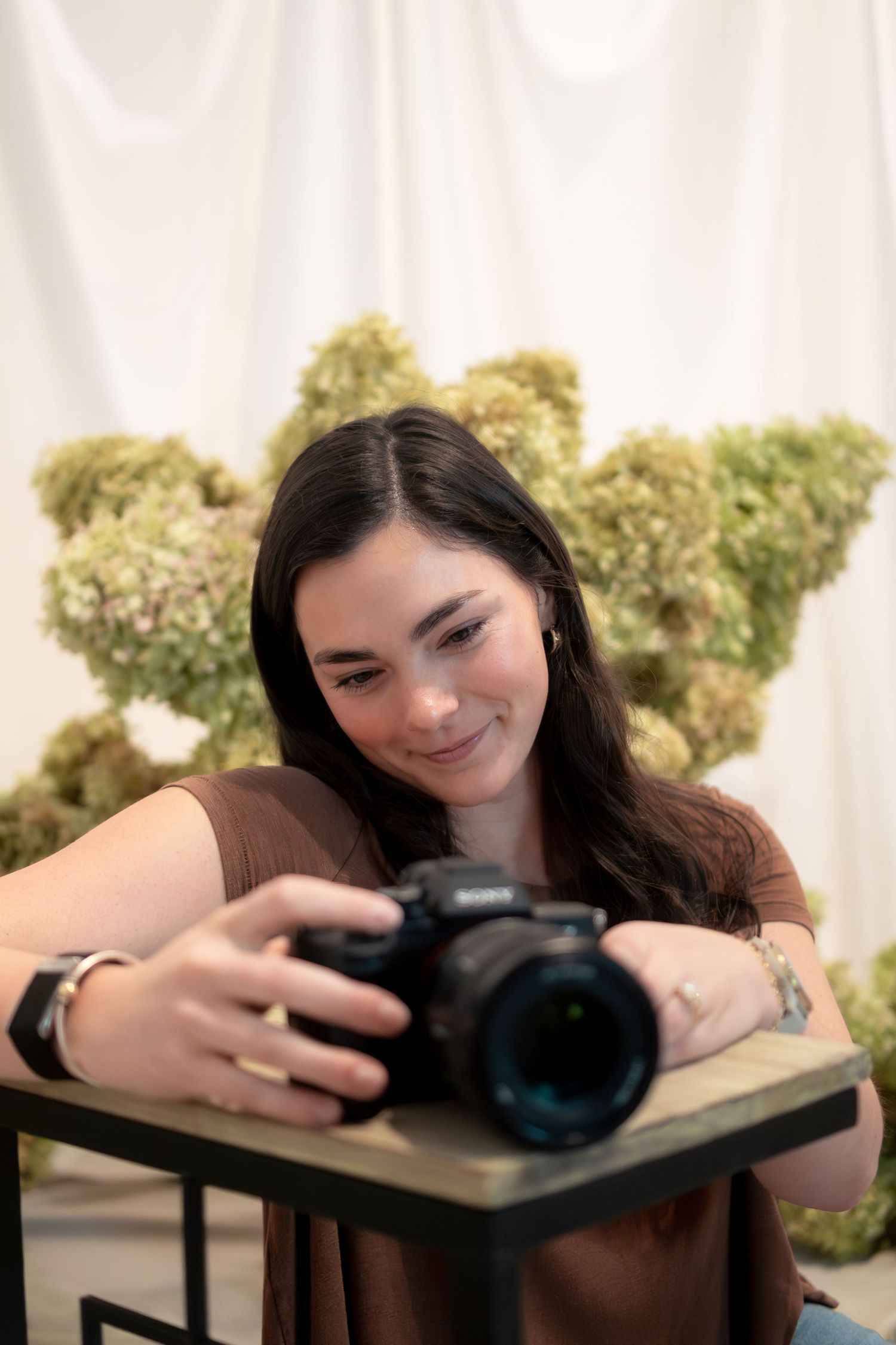 Avery Vester reviewing images on a camera against a white backdrop with dried flowers.