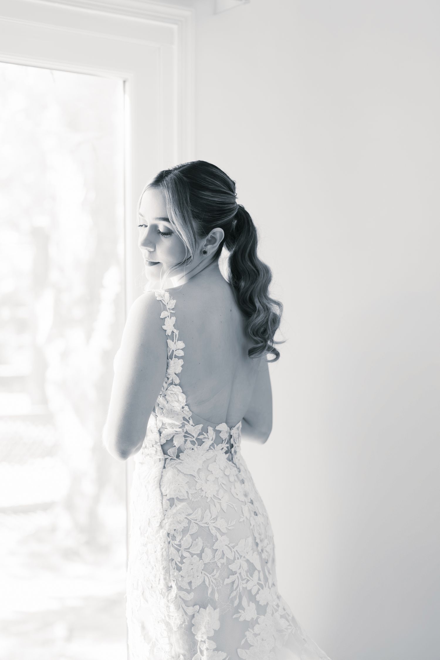 Elegant bridal portrait in black and white showing delicate lace wedding dress with floral details from behind.