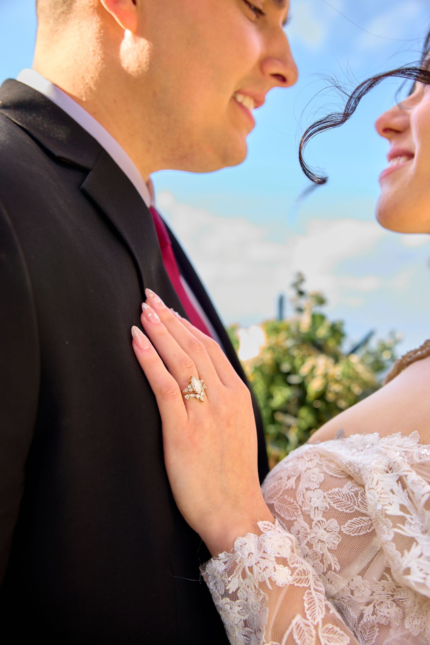 Wedding couple in formal attire sharing an intimate moment against a blue sky background.