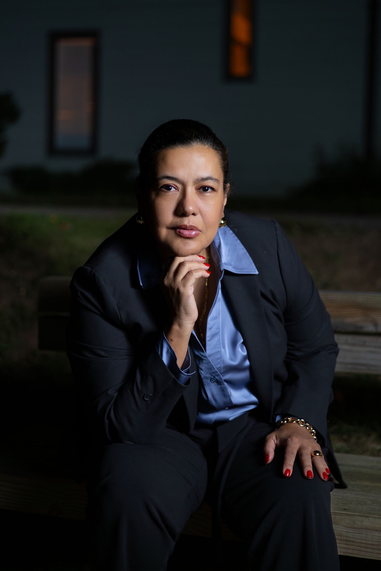 Professional business portrait in dark lighting with blue shirt and black blazer against shadowy background.