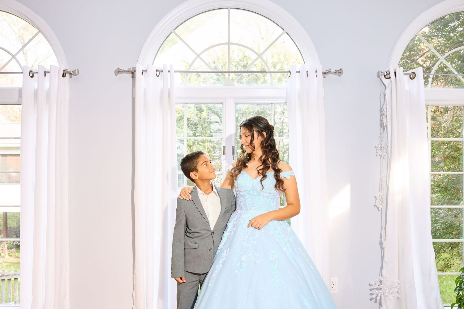 A couple shares a romantic moment in a bright sunlit room with arched windows and white walls.
