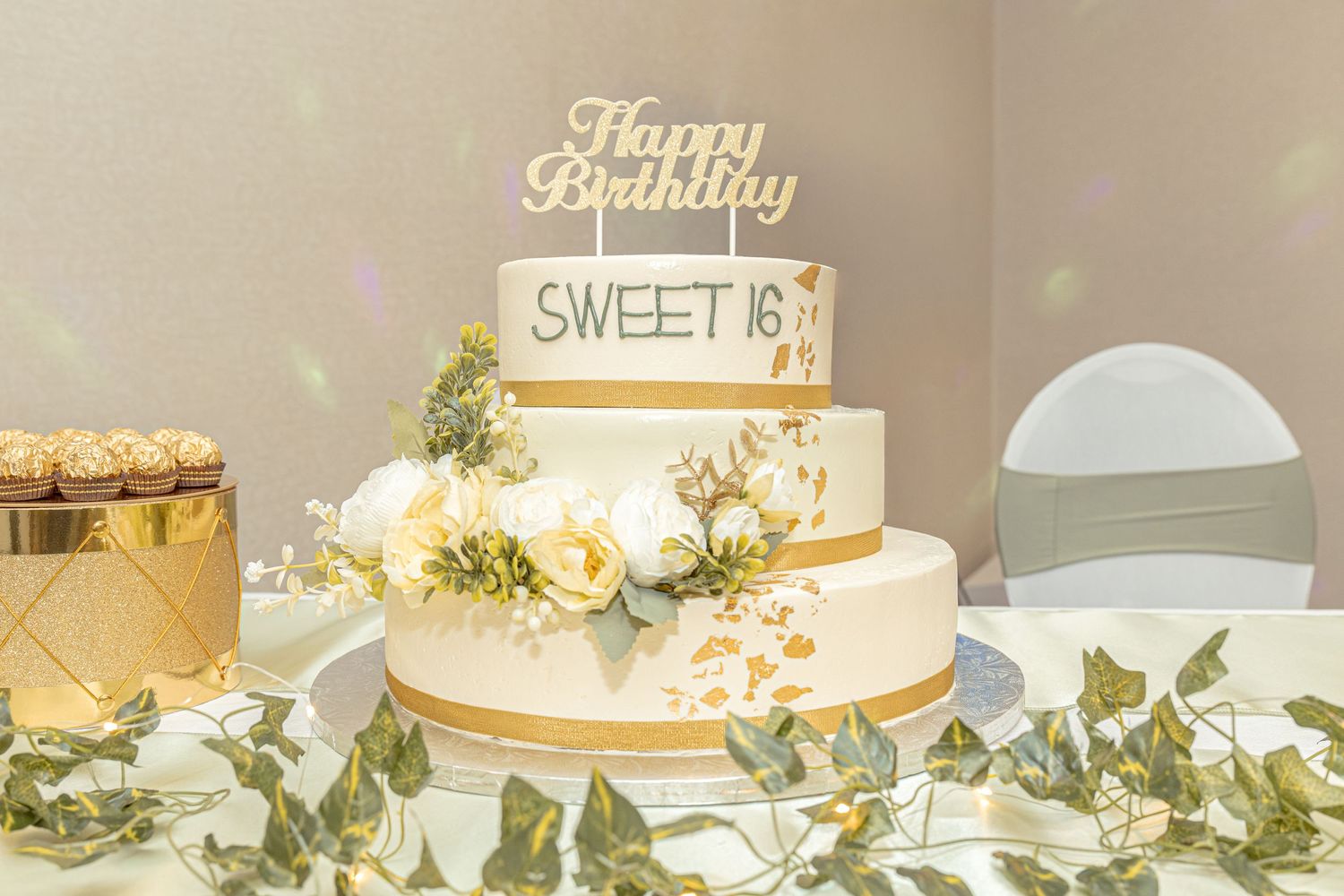 Three-tiered birthday cake with gold accents and fresh flowers.