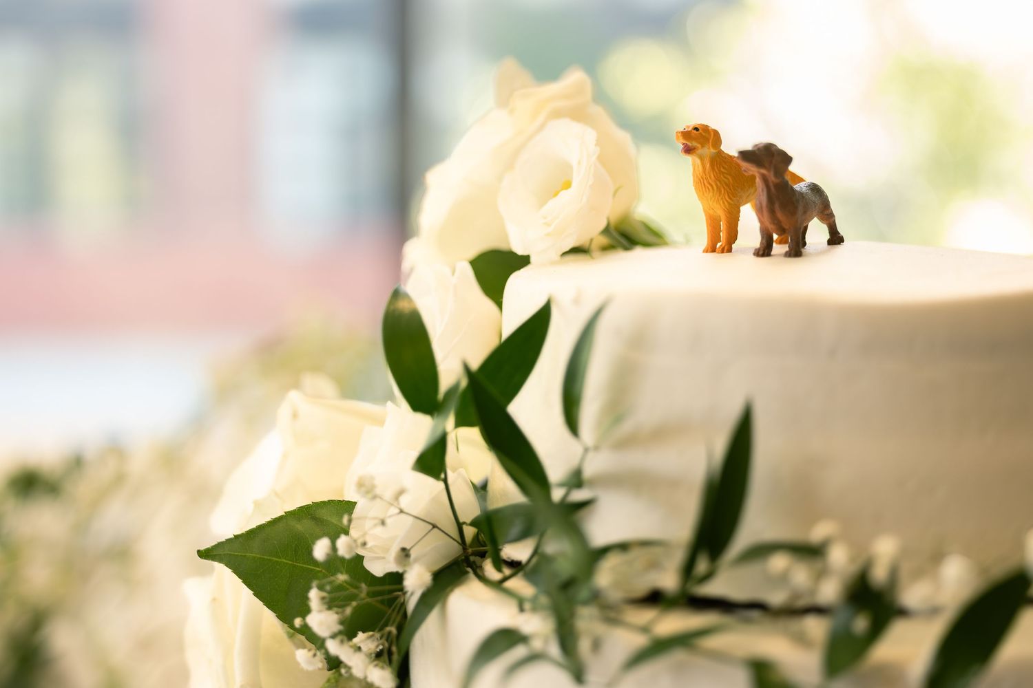 White wedding cake decorated with fresh greenery and flowers on a white tablecloth.