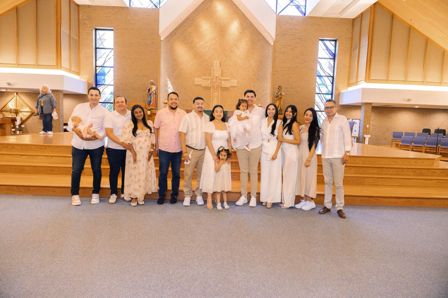 A group in coordinated white and light colored outfits stands together at the front of a modern church sanctuary.